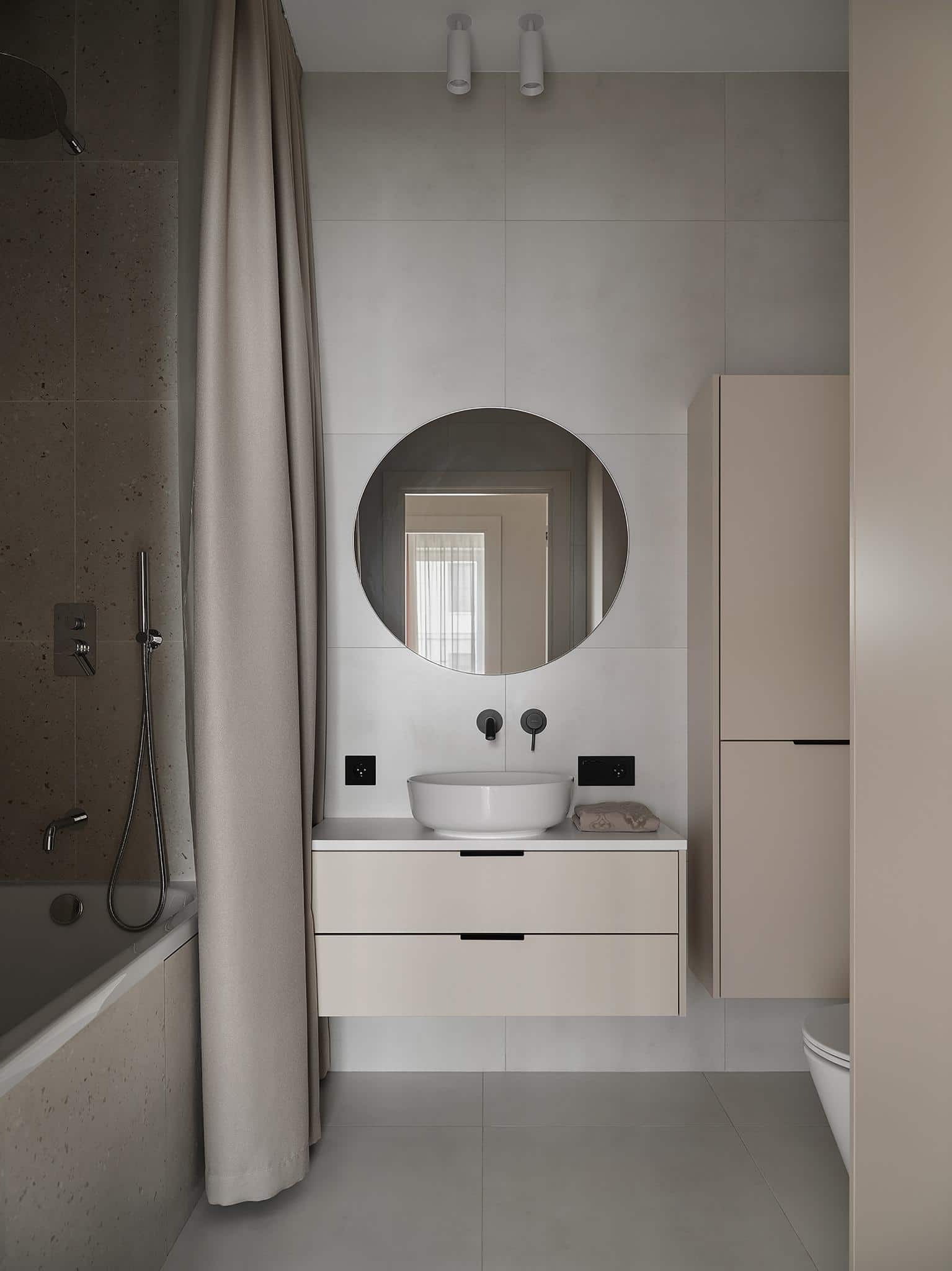 Minimalist Bathroom Design with Round Mirror Minimalist bathroom with round mirror, soft grey tiles, and neutral cabinetry.