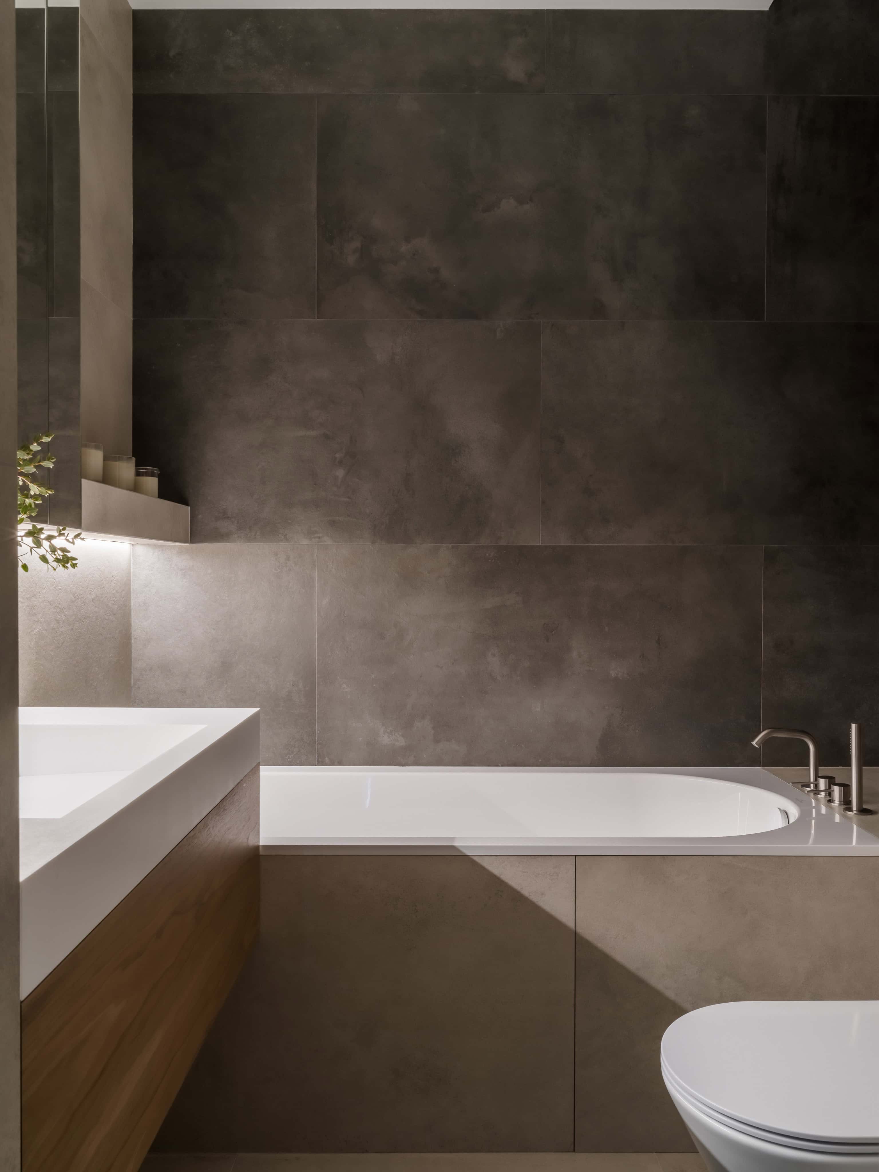 Minimalist Modern Bathroom With Tub Modern bathtub set against dark concrete-look tiles in a minimalist bathroom interior.