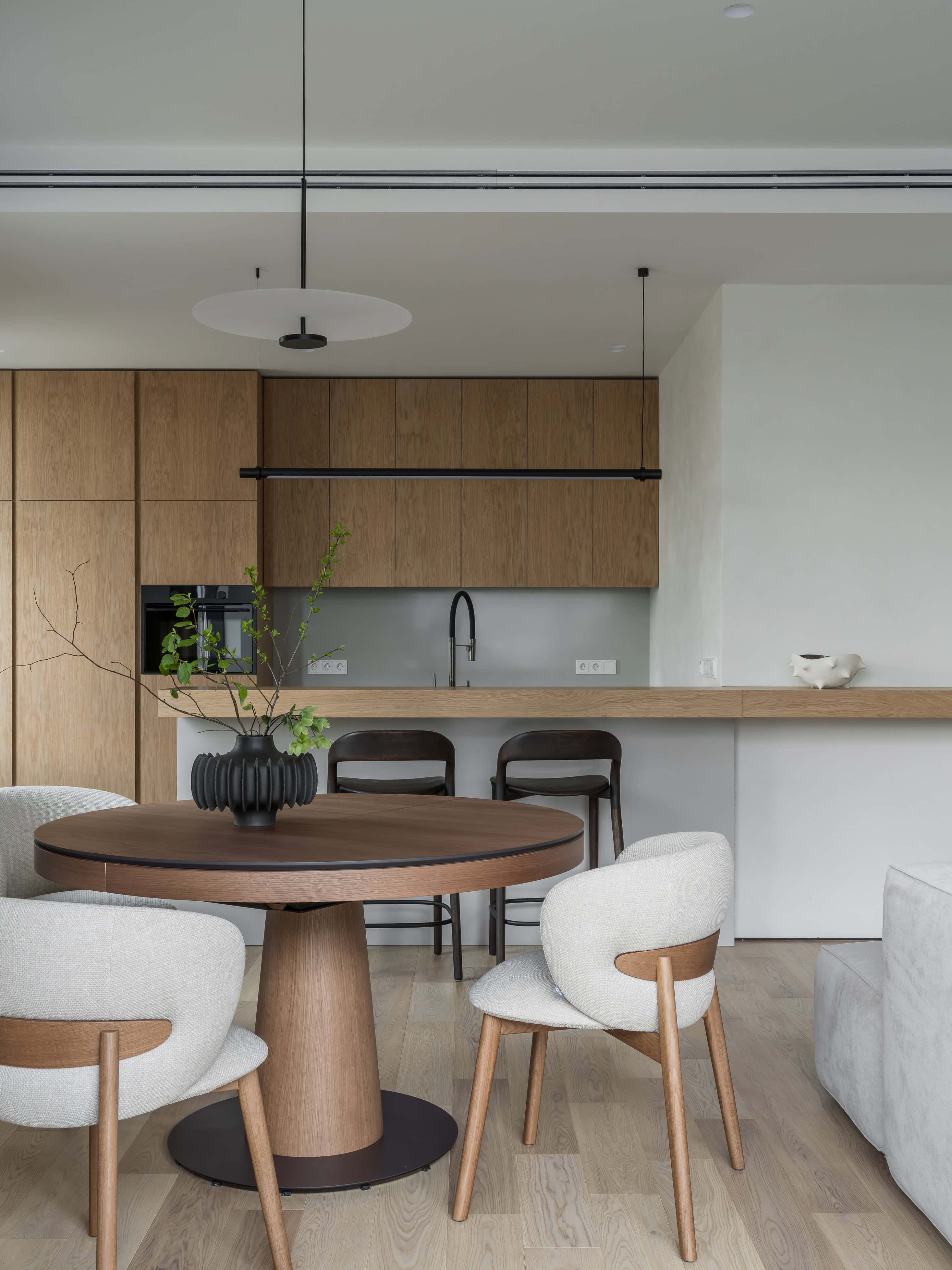 Minimalist Modern Dining Kitchen Design 2 Round wood dining table and upholstered chairs in a modern kitchen with natural lighting.