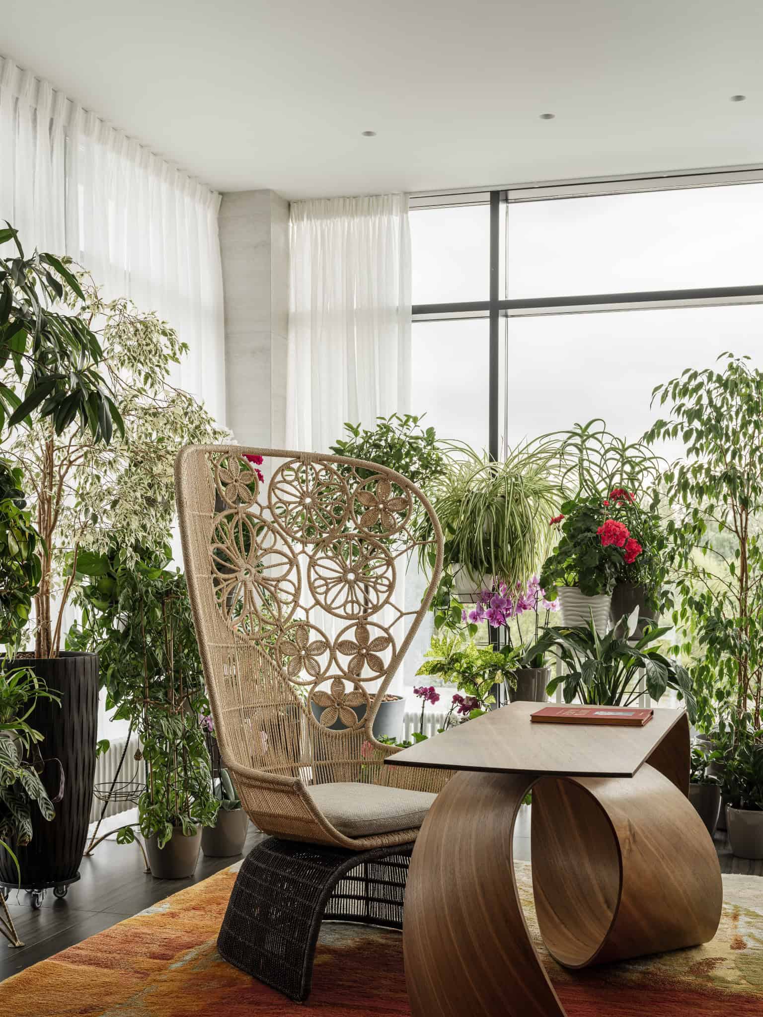 Rattan Chair in Light-Filled Garden Room Woven rattan chair in indoor garden filled with flowering plants.