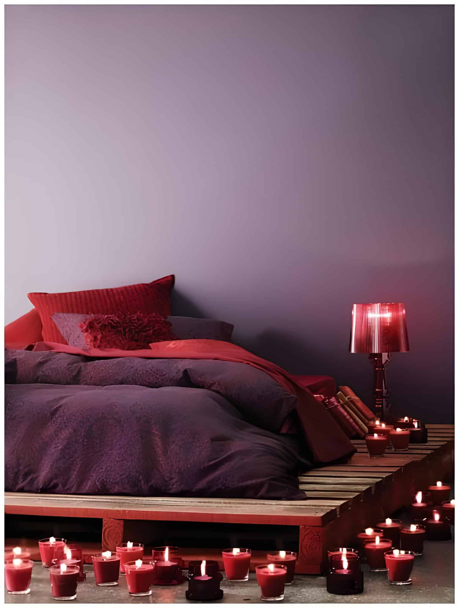 Low wooden pallet bed surrounded by glowing red candles.