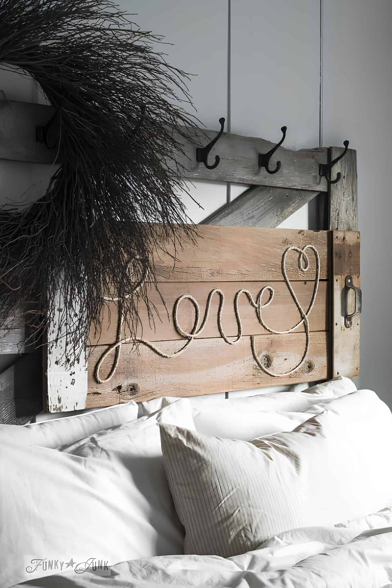 Rustic wooden sign used as a headboard, with rope spelling 'Love' and black hooks above.