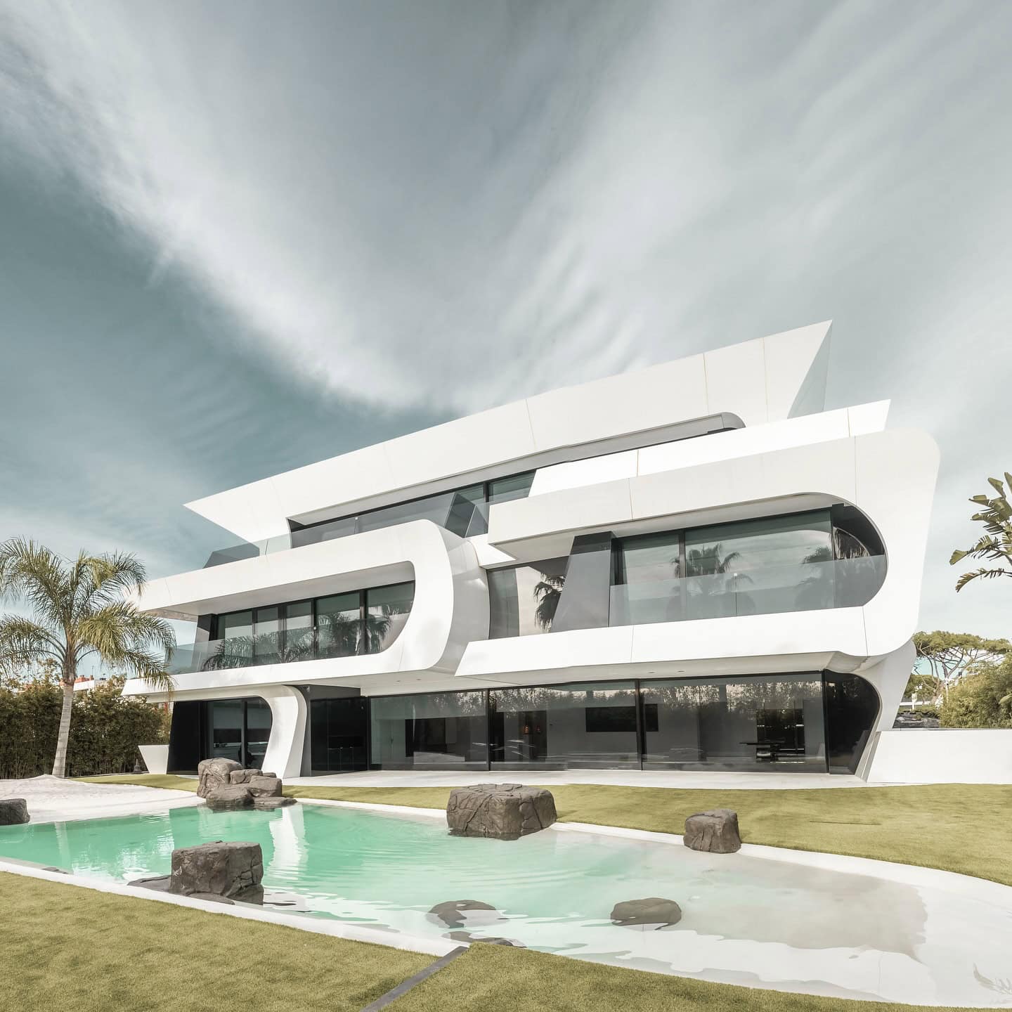Futuristic modern house with sleek white architecture, large glass windows, and a swimming pool in a lush landscape, showcasing innovative contemporary residential design.