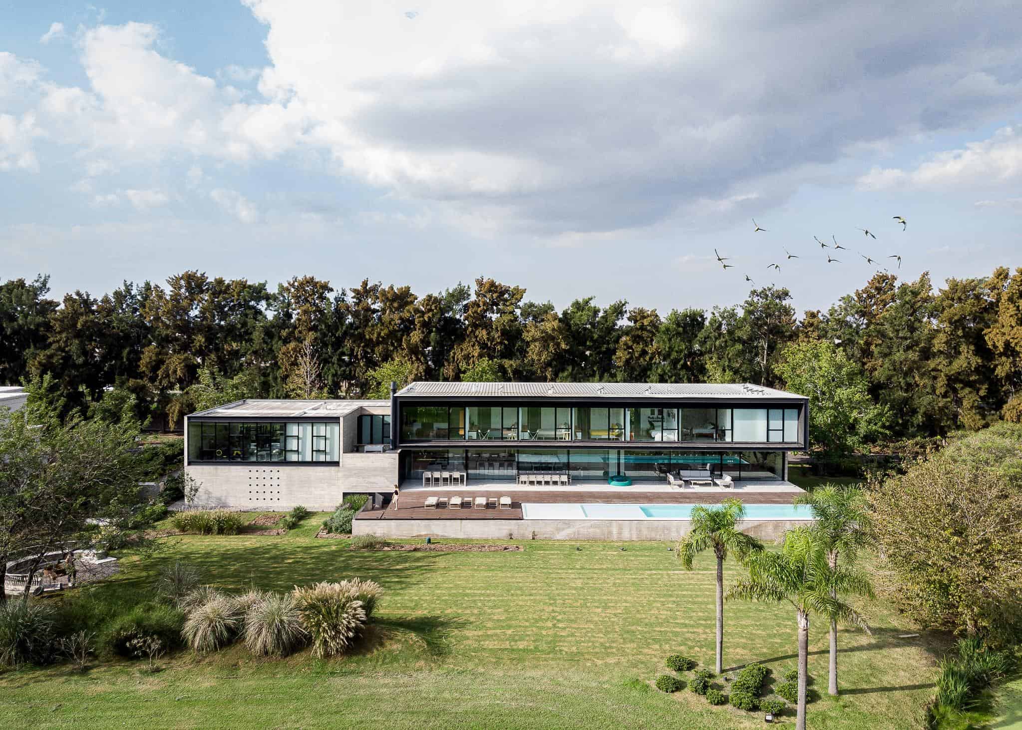 Sleek modern house with large glass windows and a swimming pool, surrounded by lush greenery and a manicured lawn, exemplifying contemporary architecture and innovative design.