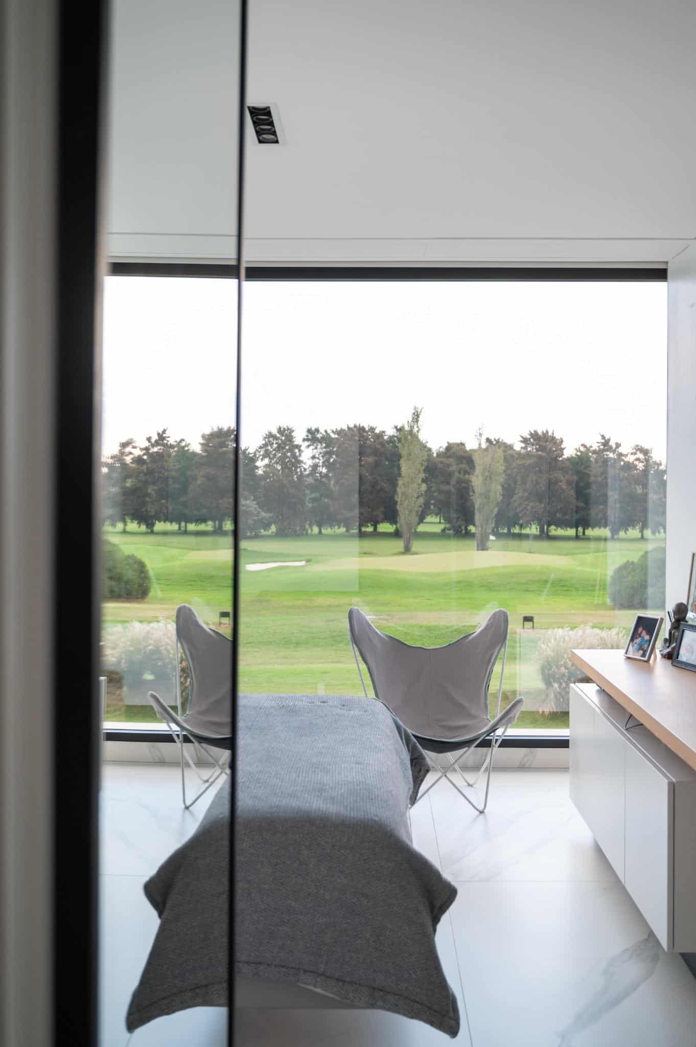 Pacheco House Bedroom with Golf View Bedroom in Pacheco House overlooking a lush green golf course through a large panoramic window.