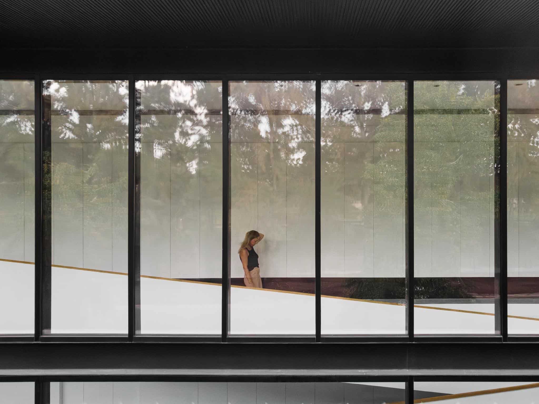 Pacheco House Glass Corridor Woman Woman walking inside the glass corridor of Pacheco House by A4estudio, surrounded by trees.