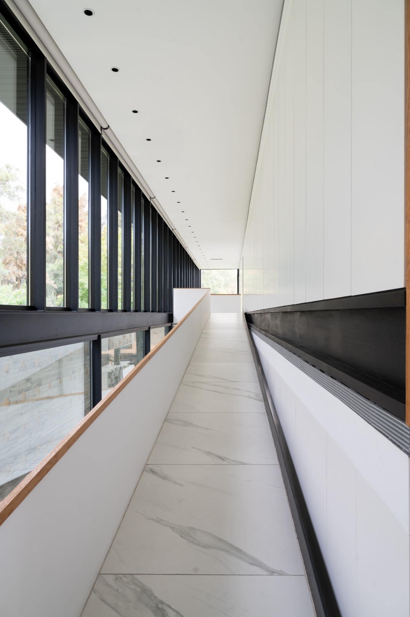 Pacheco House Hallway with Black Window Grid Modern hallway at Pacheco House featuring continuous vertical black window grid and white interior walls.