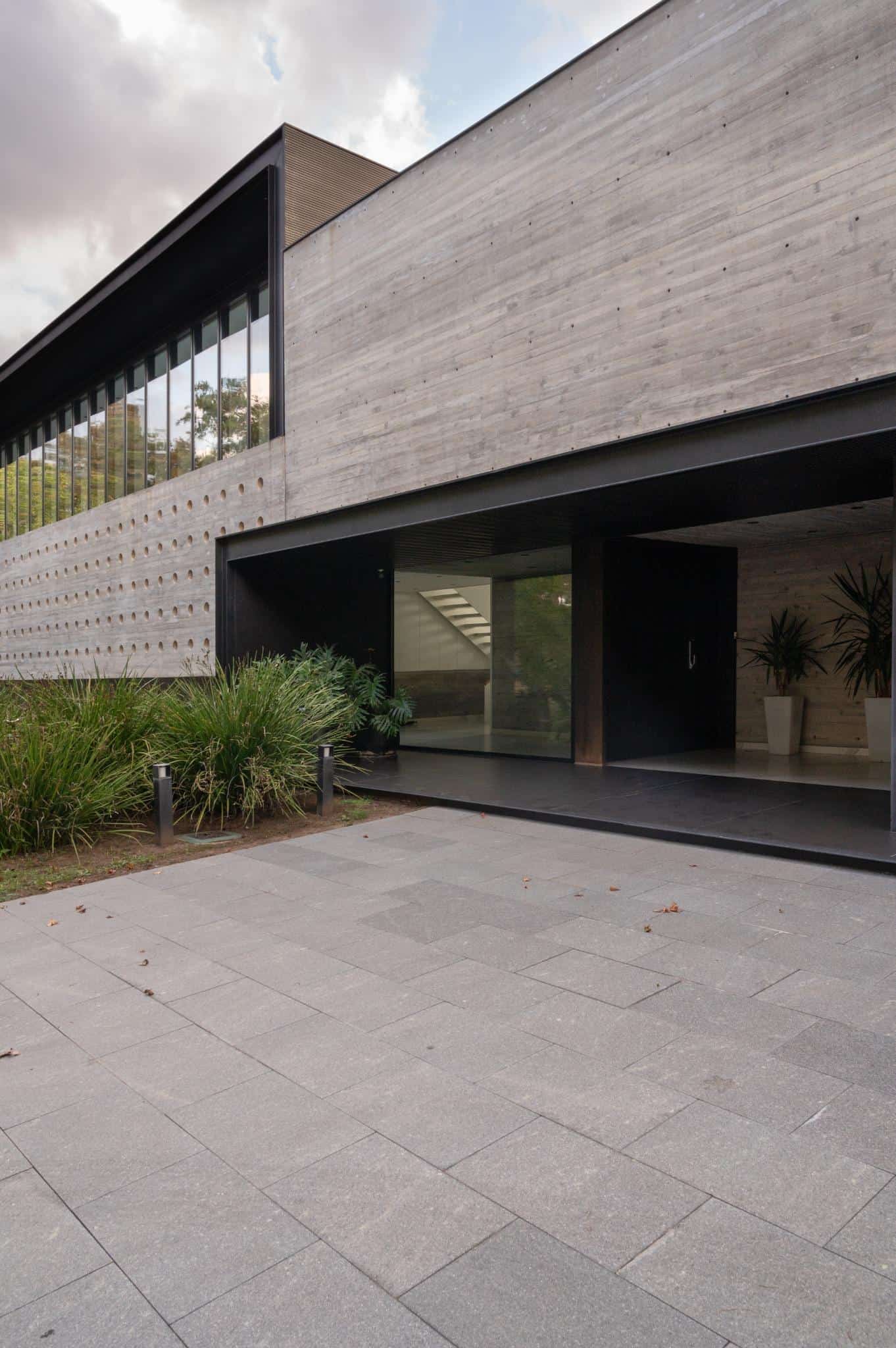Pacheco House Main Entrance Detail Close-up of the main entrance of Pacheco House with dark metal framing and lush greenery.