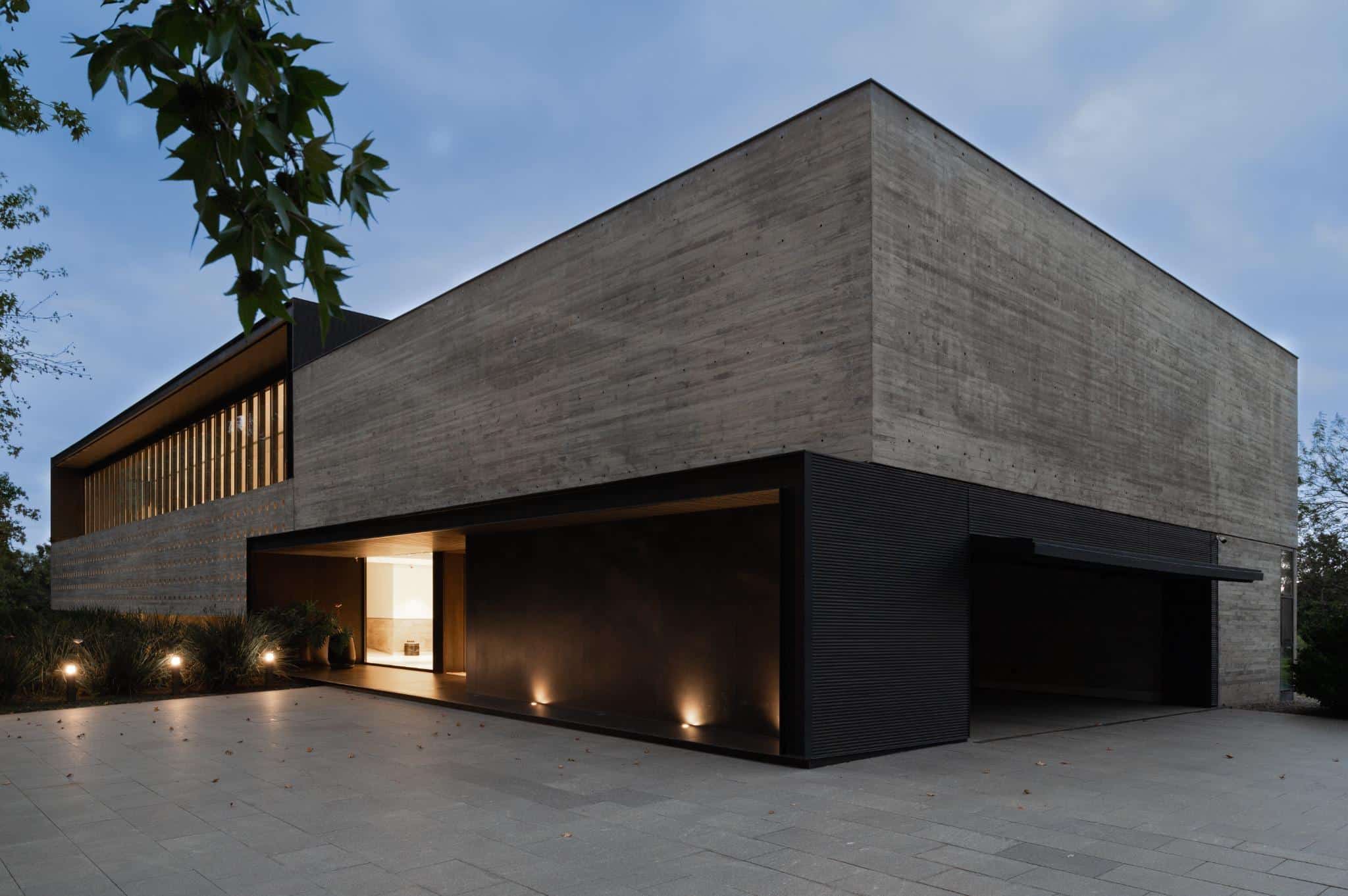 Pacheco House Night Exterior Driveway View Exterior nighttime perspective of Pacheco House featuring minimalist lighting and bold concrete geometry.