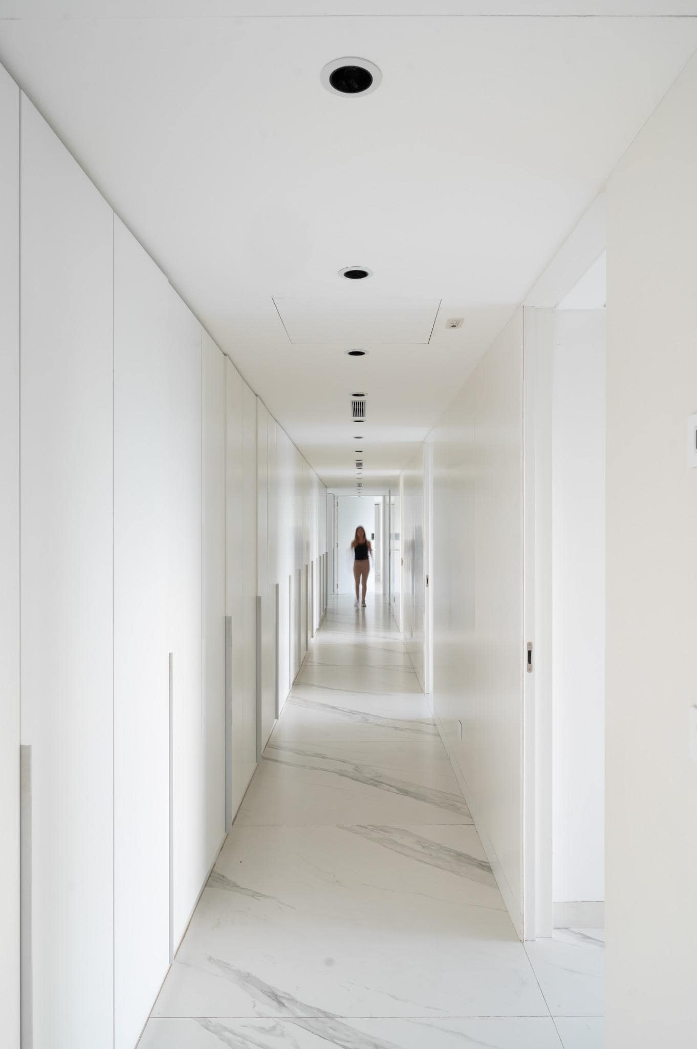 Pacheco House White Hallway Design Long minimalist hallway in Pacheco House featuring seamless white walls and marble-effect flooring.