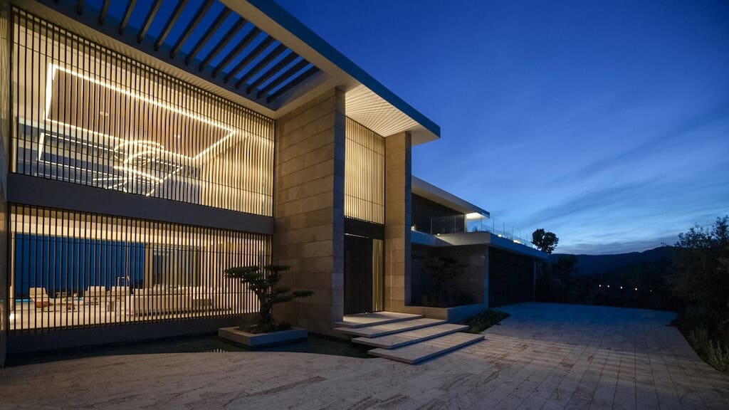 Villa Kaizen Front Facade Dusk Front elevation of Villa Kaizen lit at dusk, showcasing vertical louvers and clean geometry.