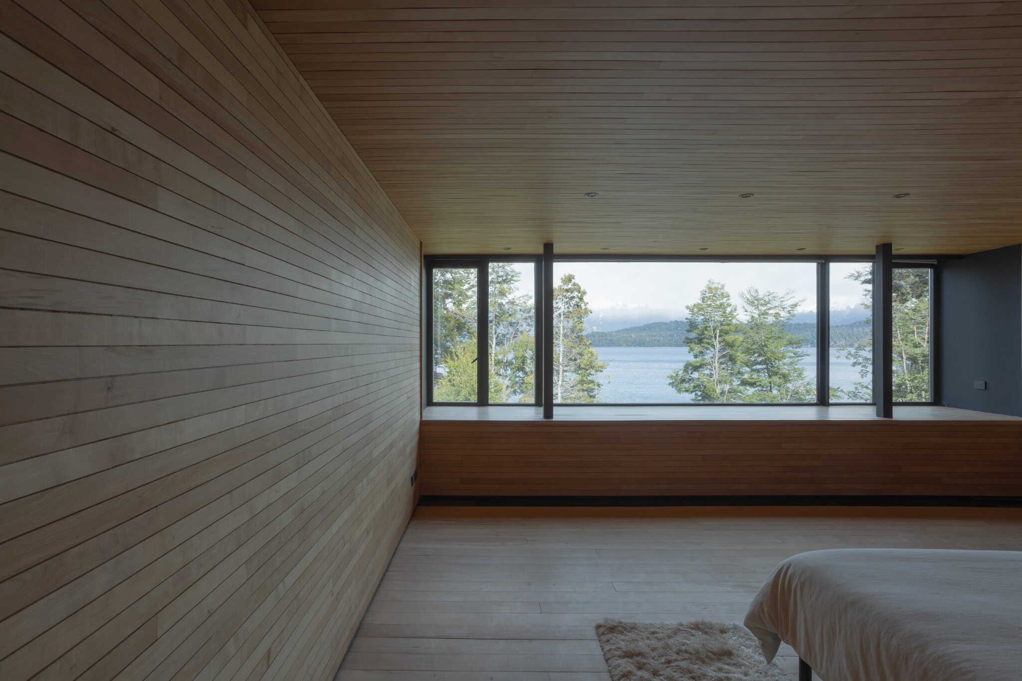 Panoramic glass window in bedroom of VLA House with view to lake and trees.
