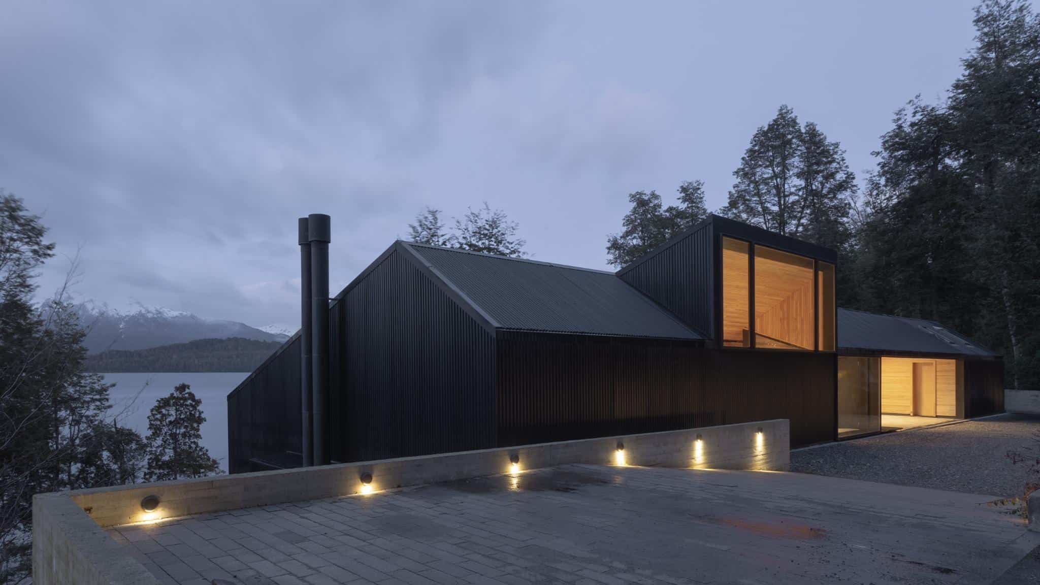 VLA House by A4estudio with illuminated black facade and wooden entrance.