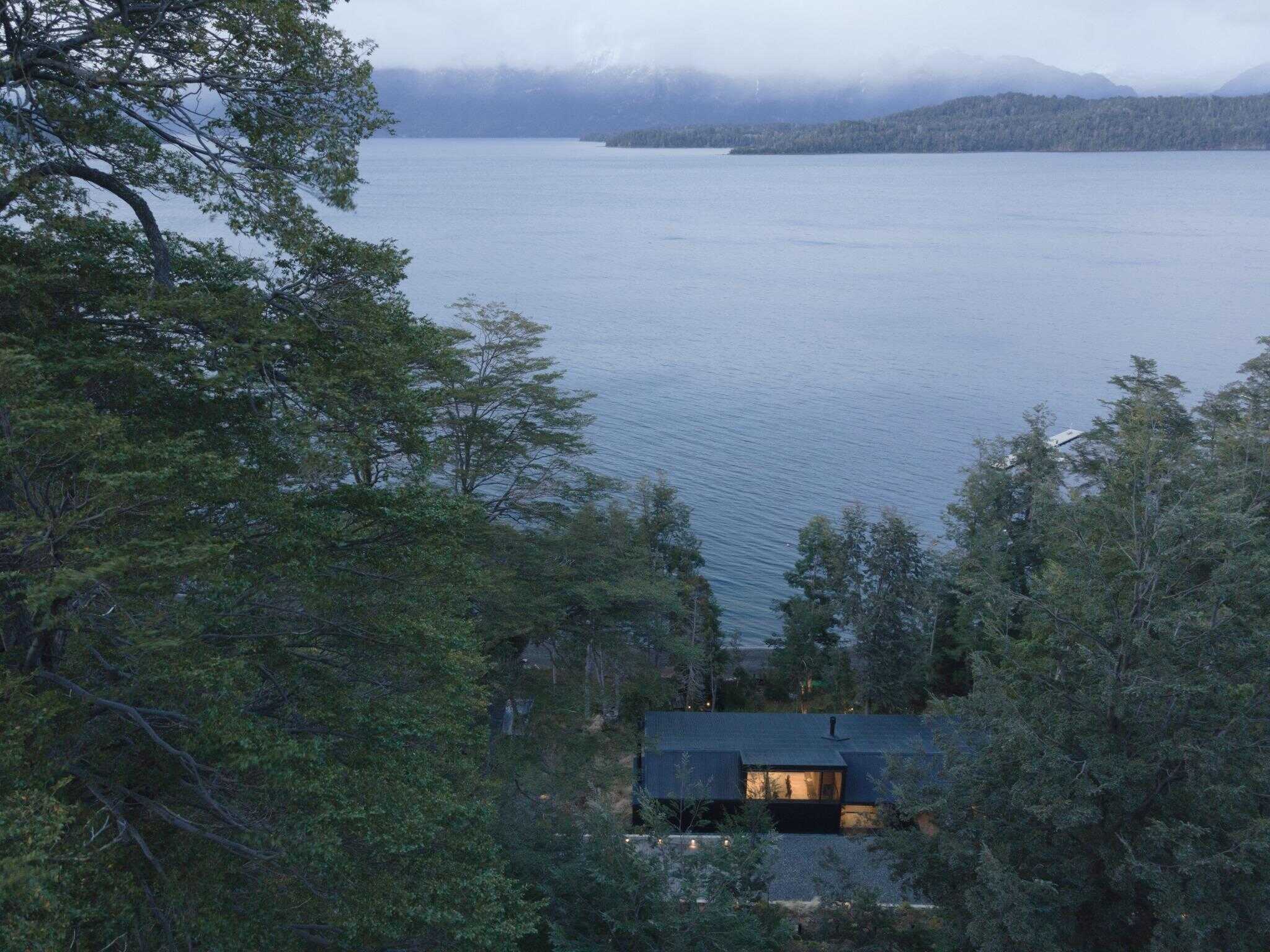 VLA House by A4estudio viewed across lake in forest setting.