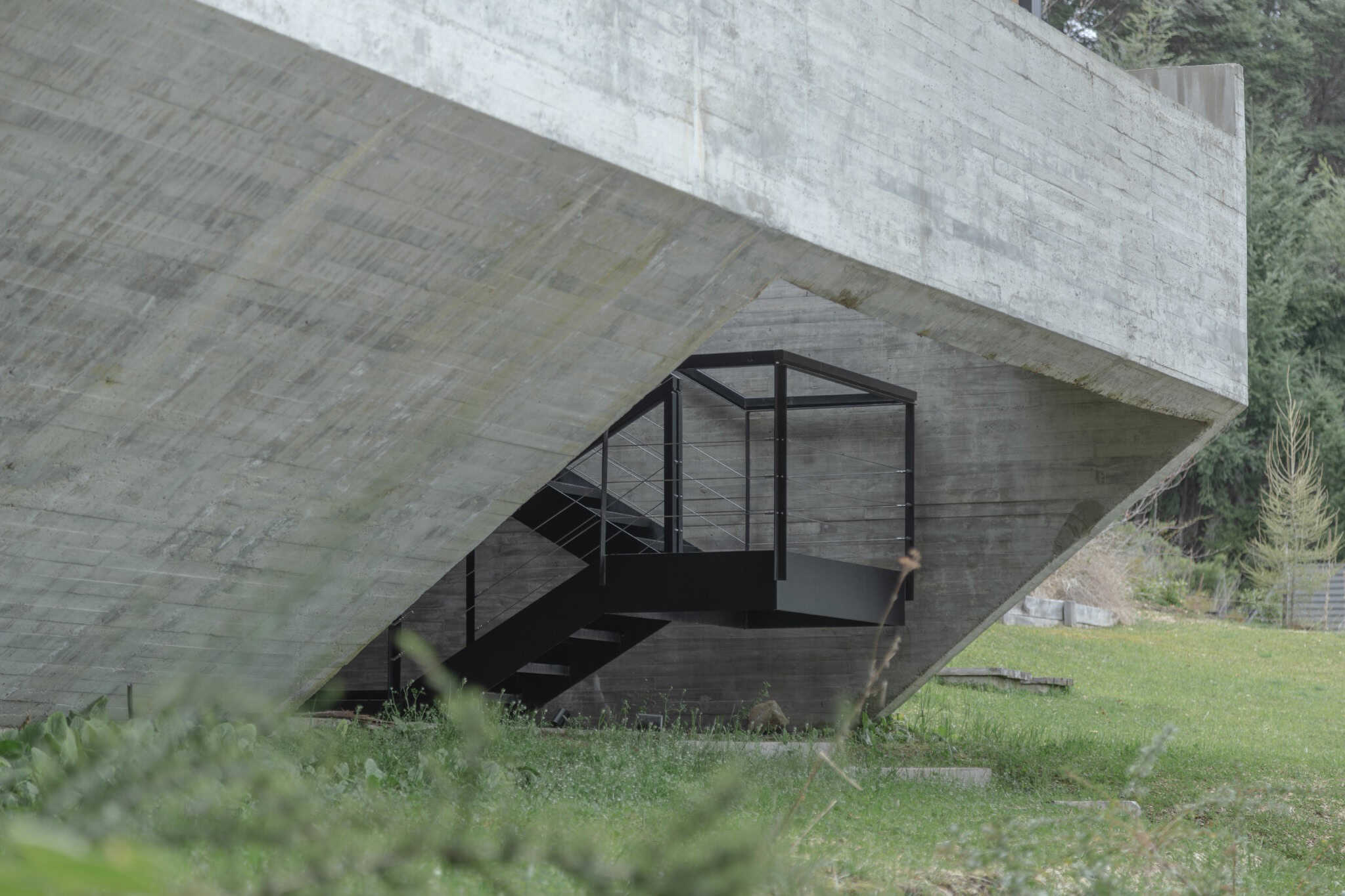 Understructure of VLA House with exposed concrete and black staircase.