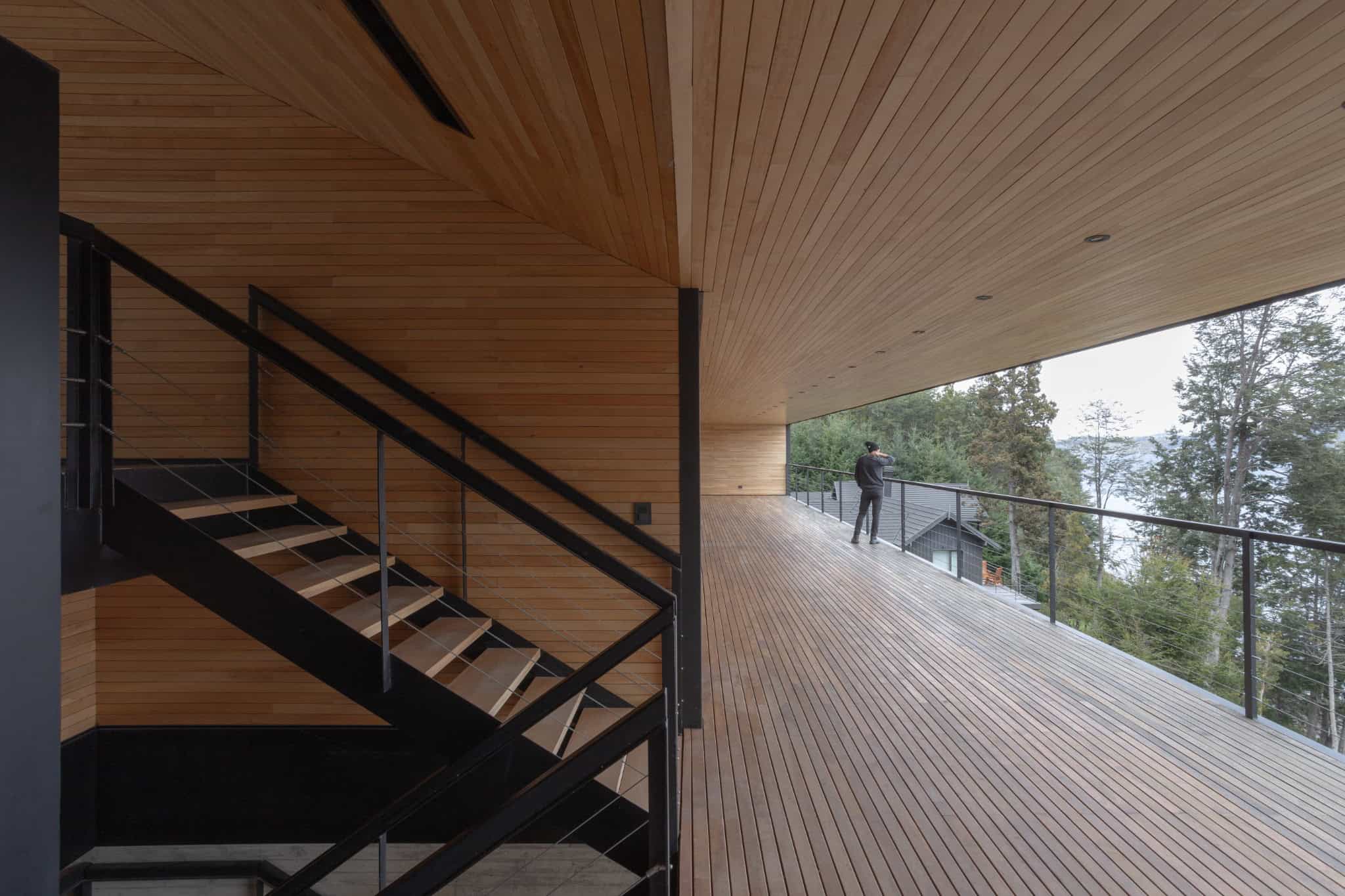Covered deck and metal staircase view overlooking trees and lake at VLA House.