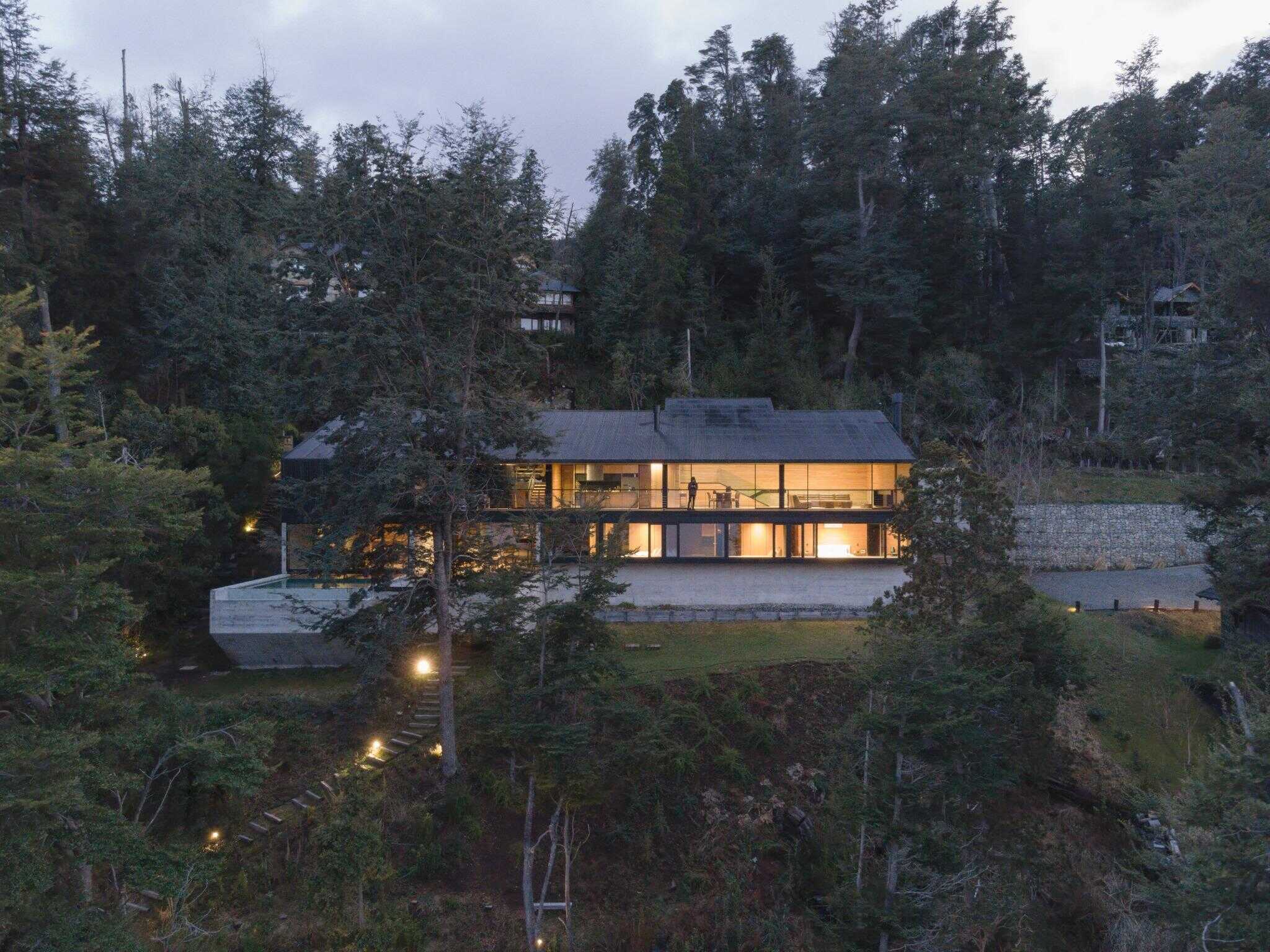 Front facade of VLA House by A4estudio illuminated in forest clearing.