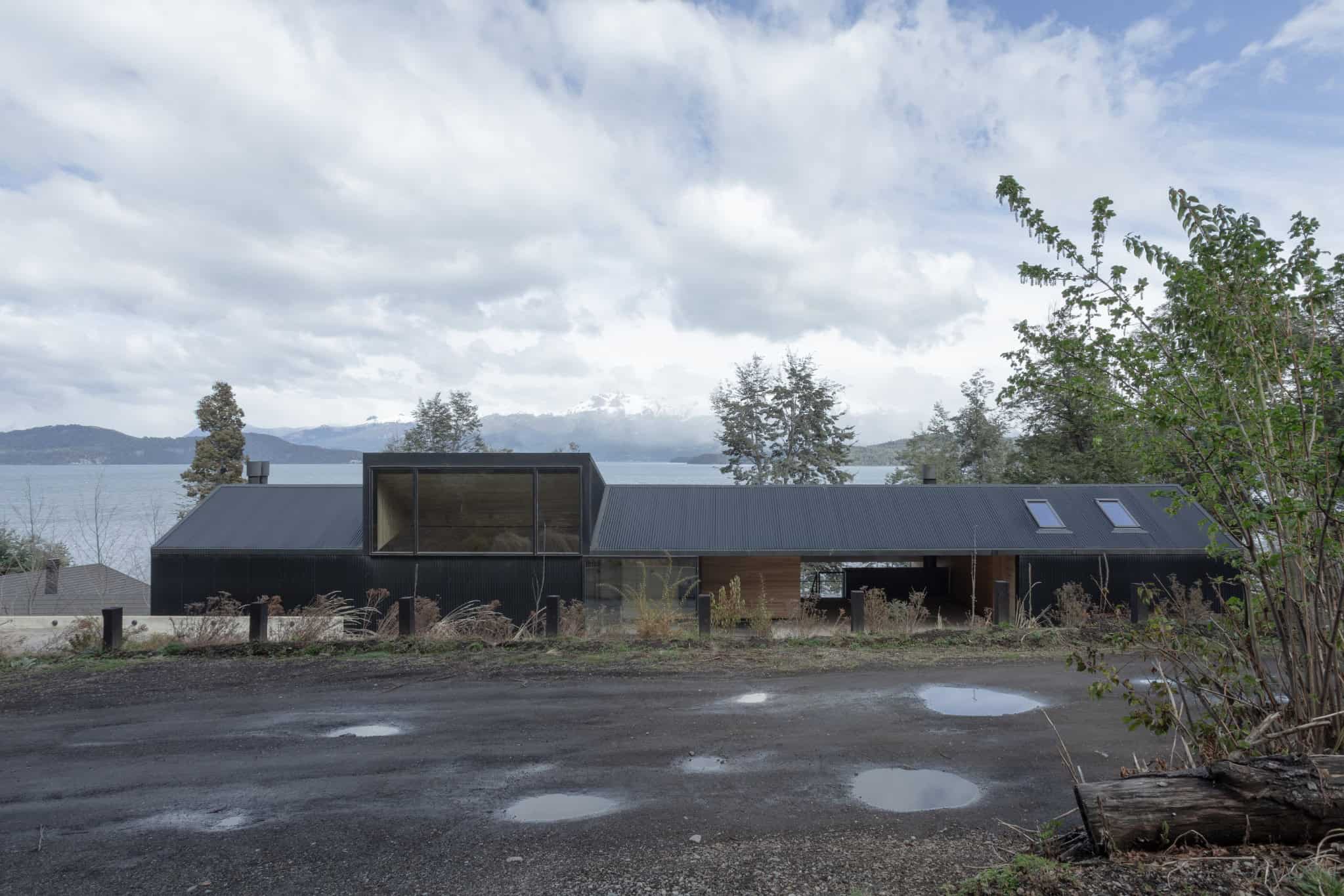 Modern black minimalist house with large glass windows and a sloped metal roof set against a natural lakeside landscape.