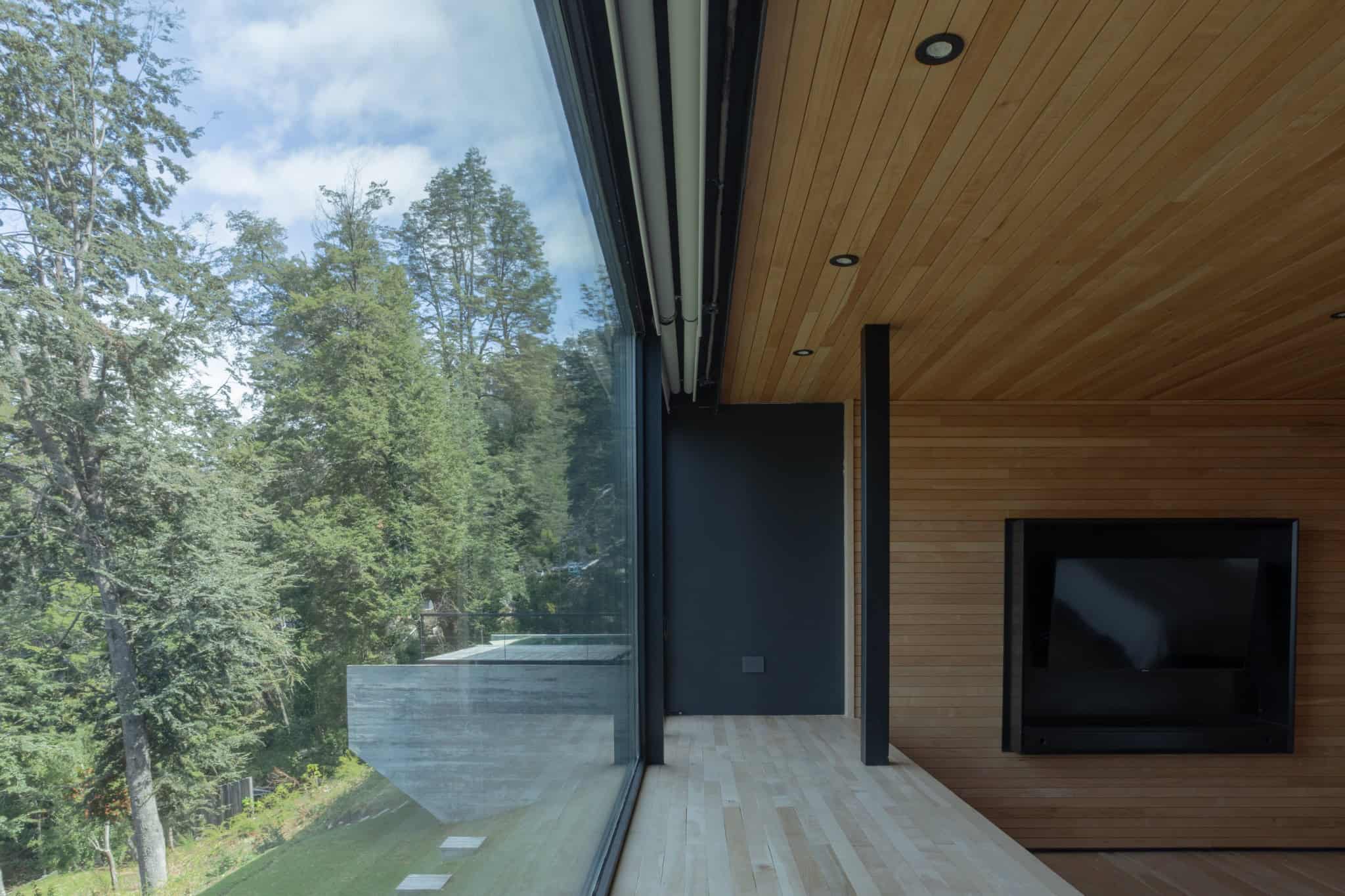 Glass corner wall in VLA House bedroom revealing lush forest and pool roof.