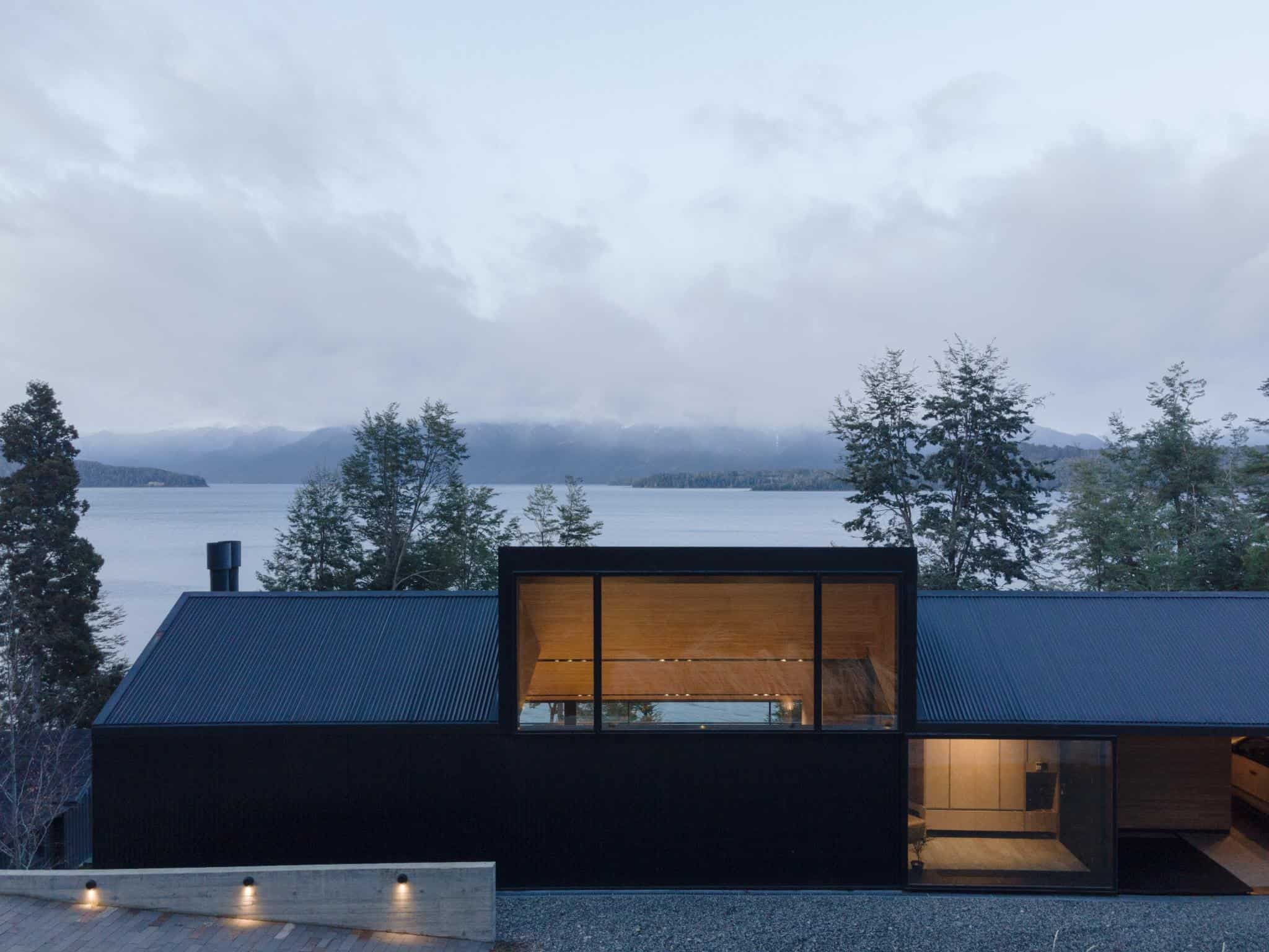 Lakefront elevation of VLA House by A4estudio showing dark exterior and full-height windows.
