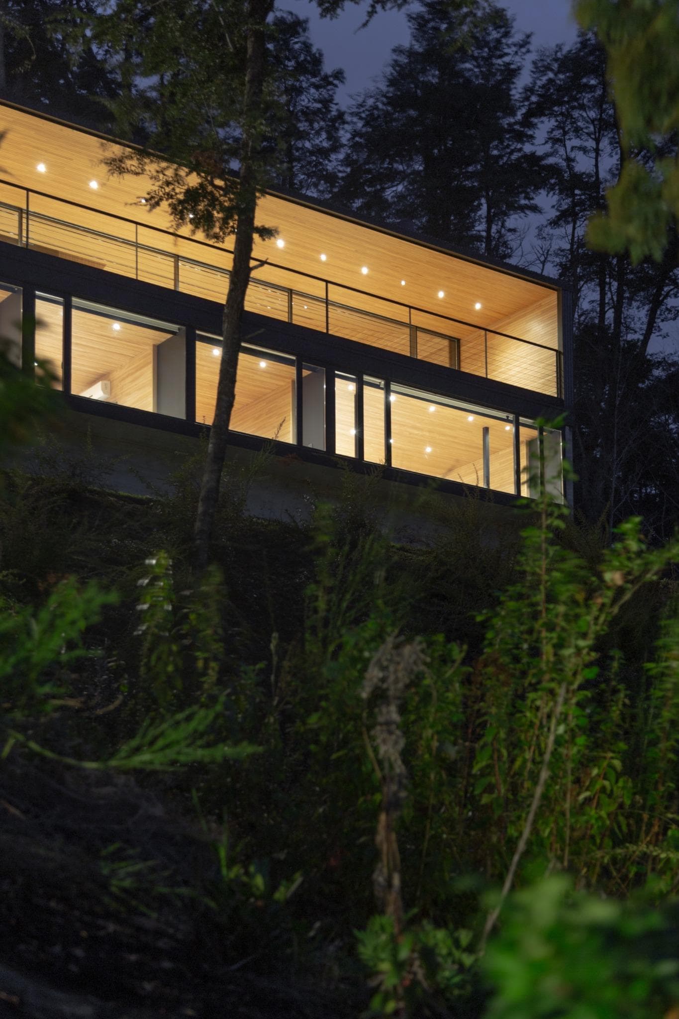 Upper balcony of VLA House by A4estudio glowing through the forest at night.
