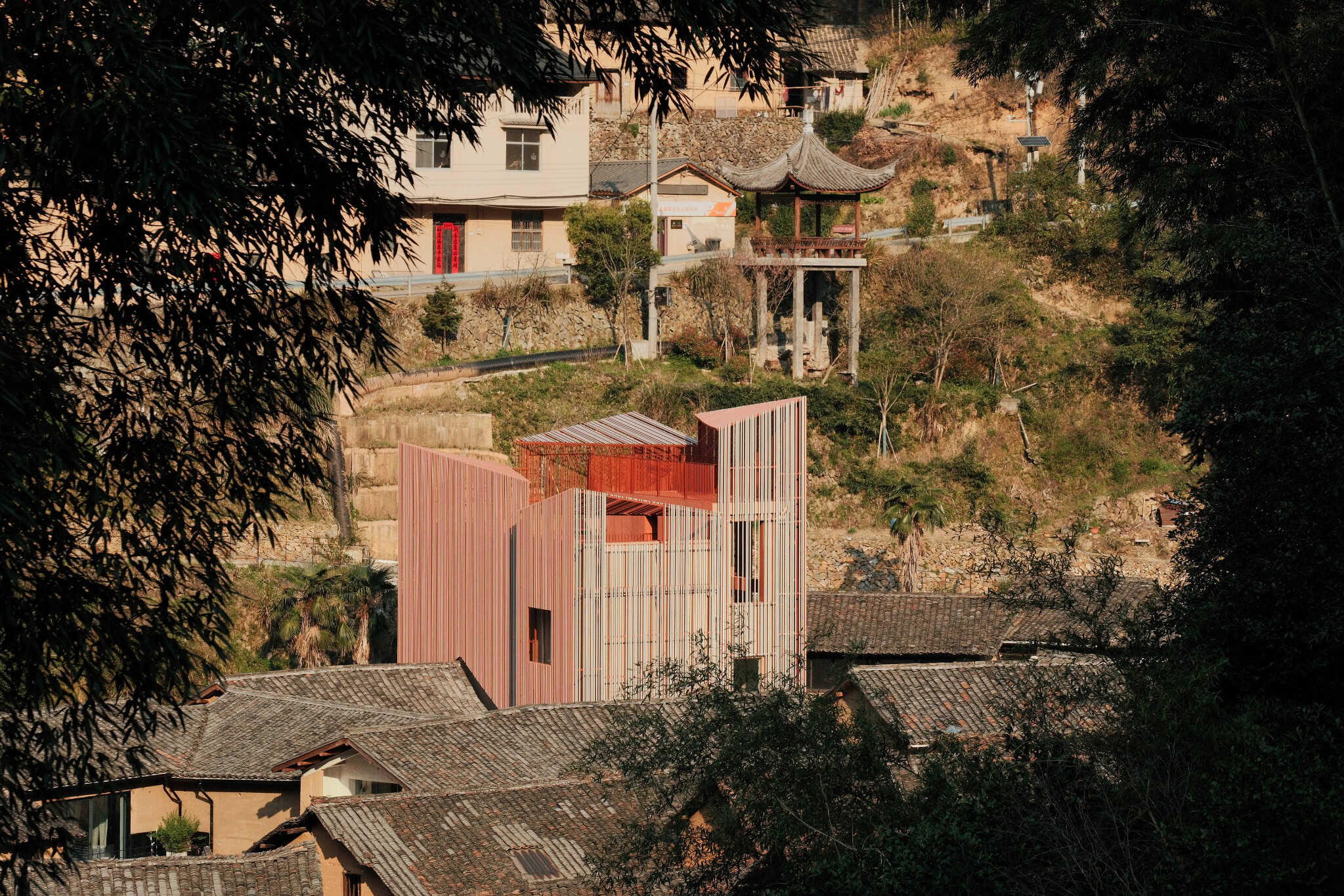 Modern architectural building with vertical red and white facade set against hillside landscape in a rural area, showcasing innovative design and integration with natural environment.
