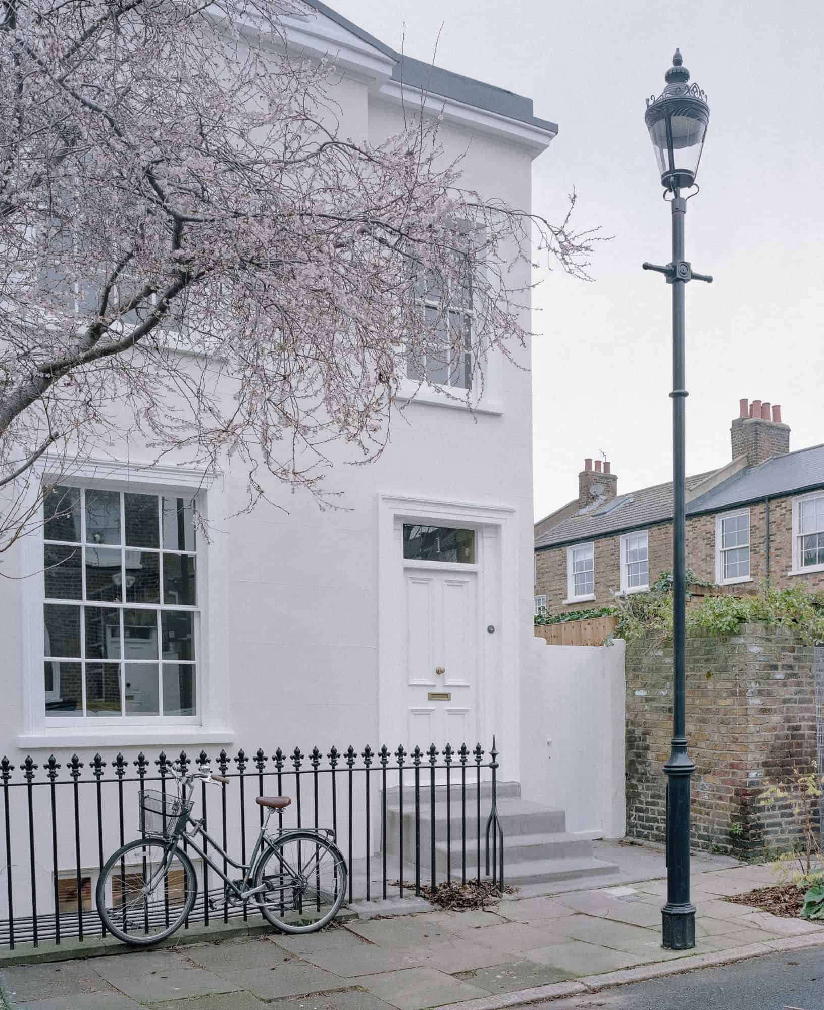 Vintage black bicycle parked in front of a charming white house with classic architecture and street lamp, showcasing city street design and residential architecture.
