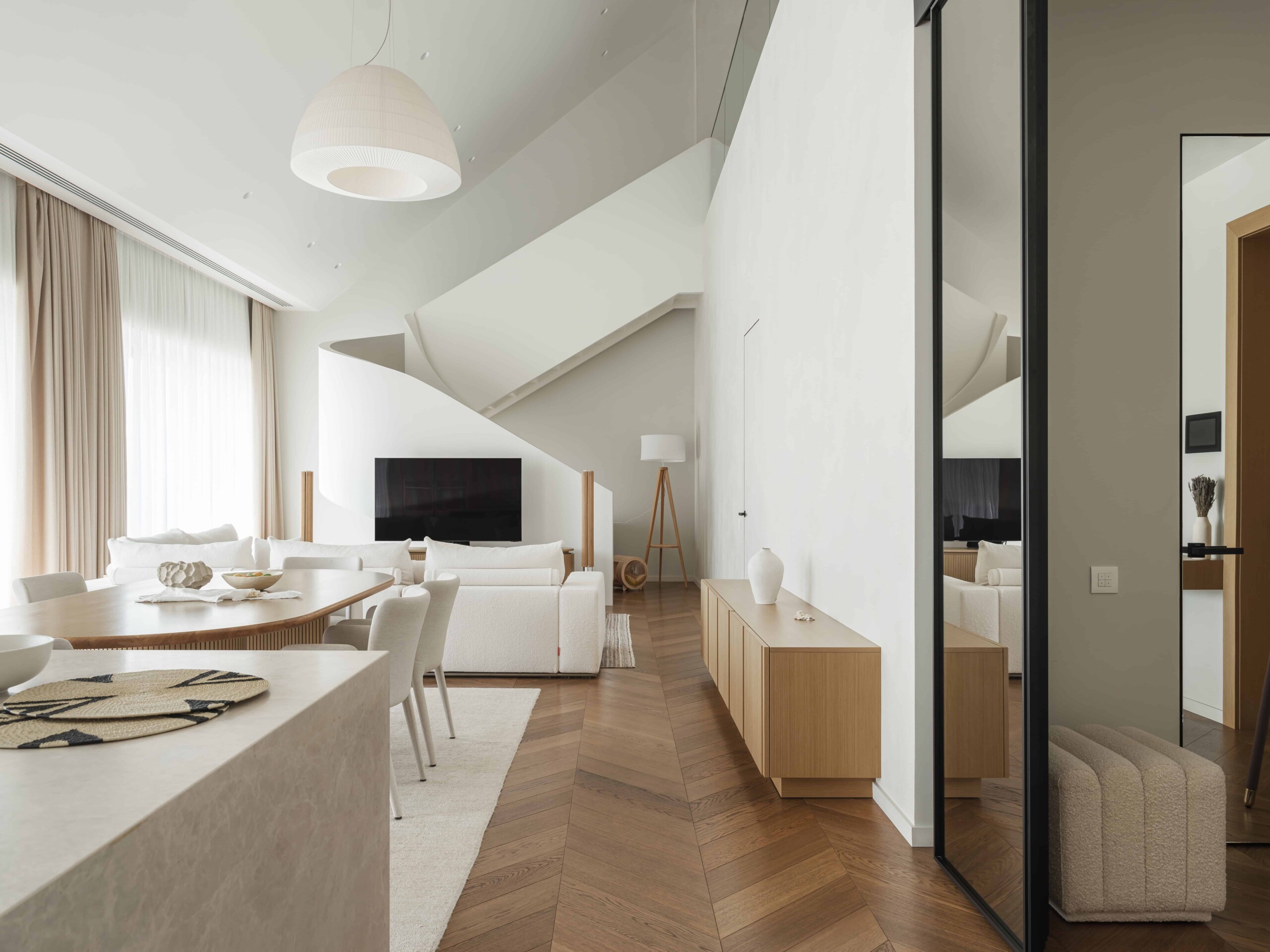 Modern minimalist living room with white furniture, wooden accents, and large windows with beige curtains. Open-concept design featuring clean lines, contemporary decor, and natural light.