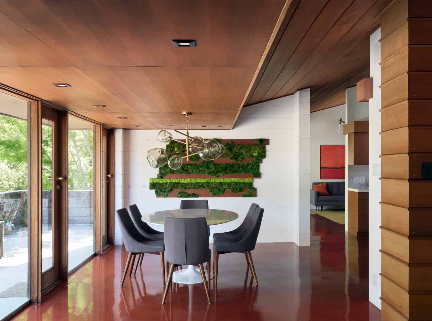 Modern interior dining area with wood accents, green living wall, and contemporary décor, featuring natural sunlight, stylish lighting fixtures, and seamless outdoor view.