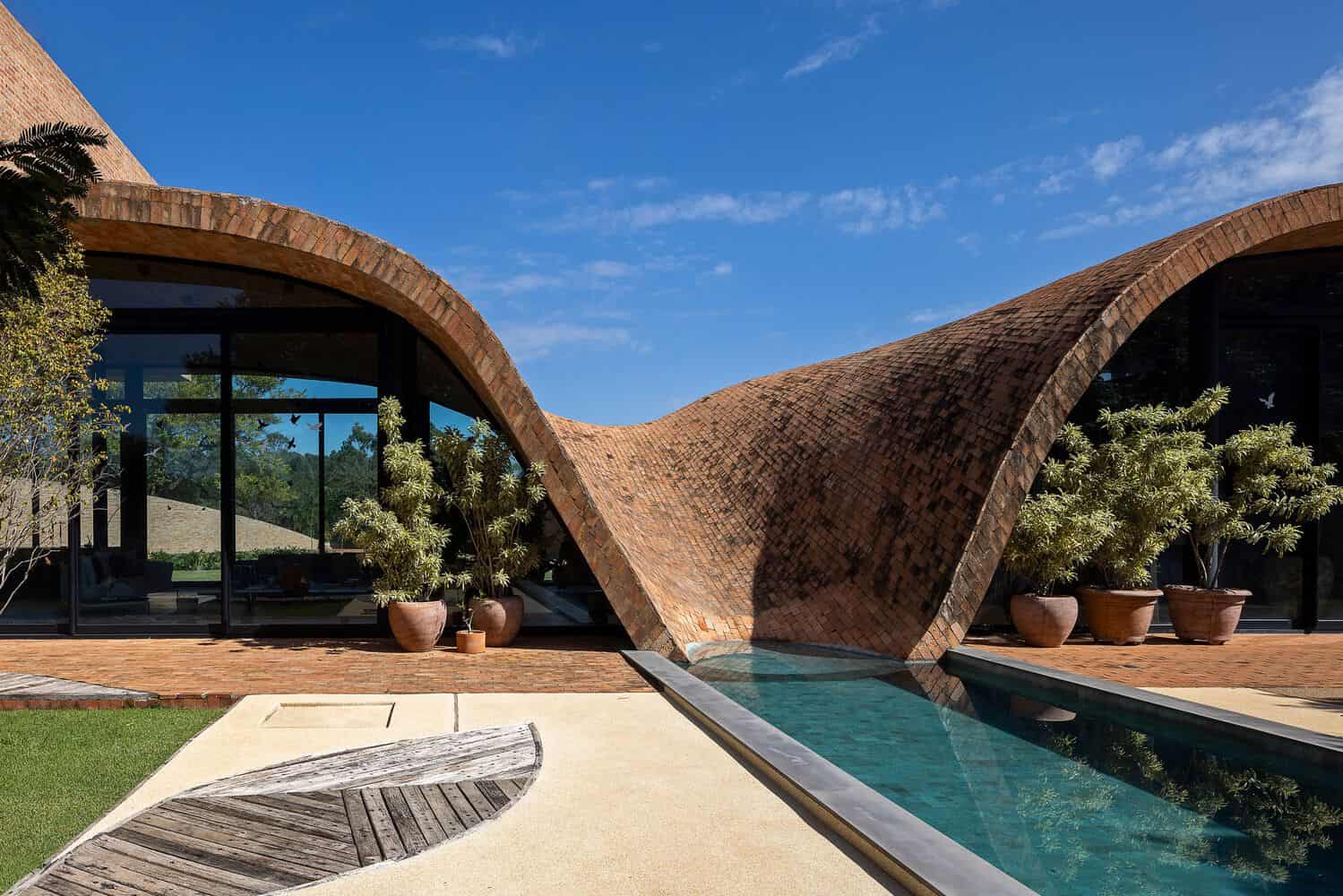 Passive House Pool Curved Brick Wall by Mareines Arquitetura Contemporary modern house with unique curved brick architecture and an outdoor pool, surrounded by potted plants and lush greenery, showcasing innovative design and stylish outdoor living spaces.