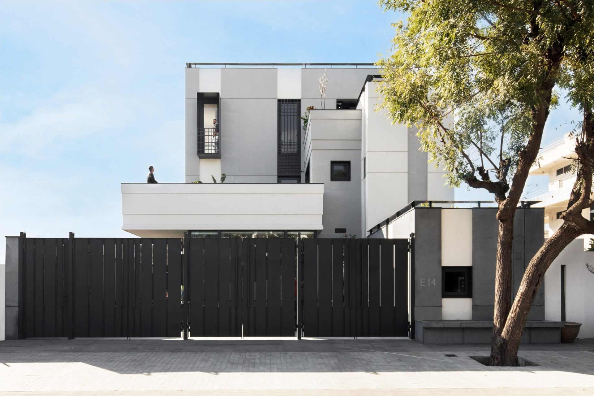Contemporary modern white house with sleek architecture, black accents, and spacious outdoor terrace, surrounded by stylish black fencing and lush greenery.