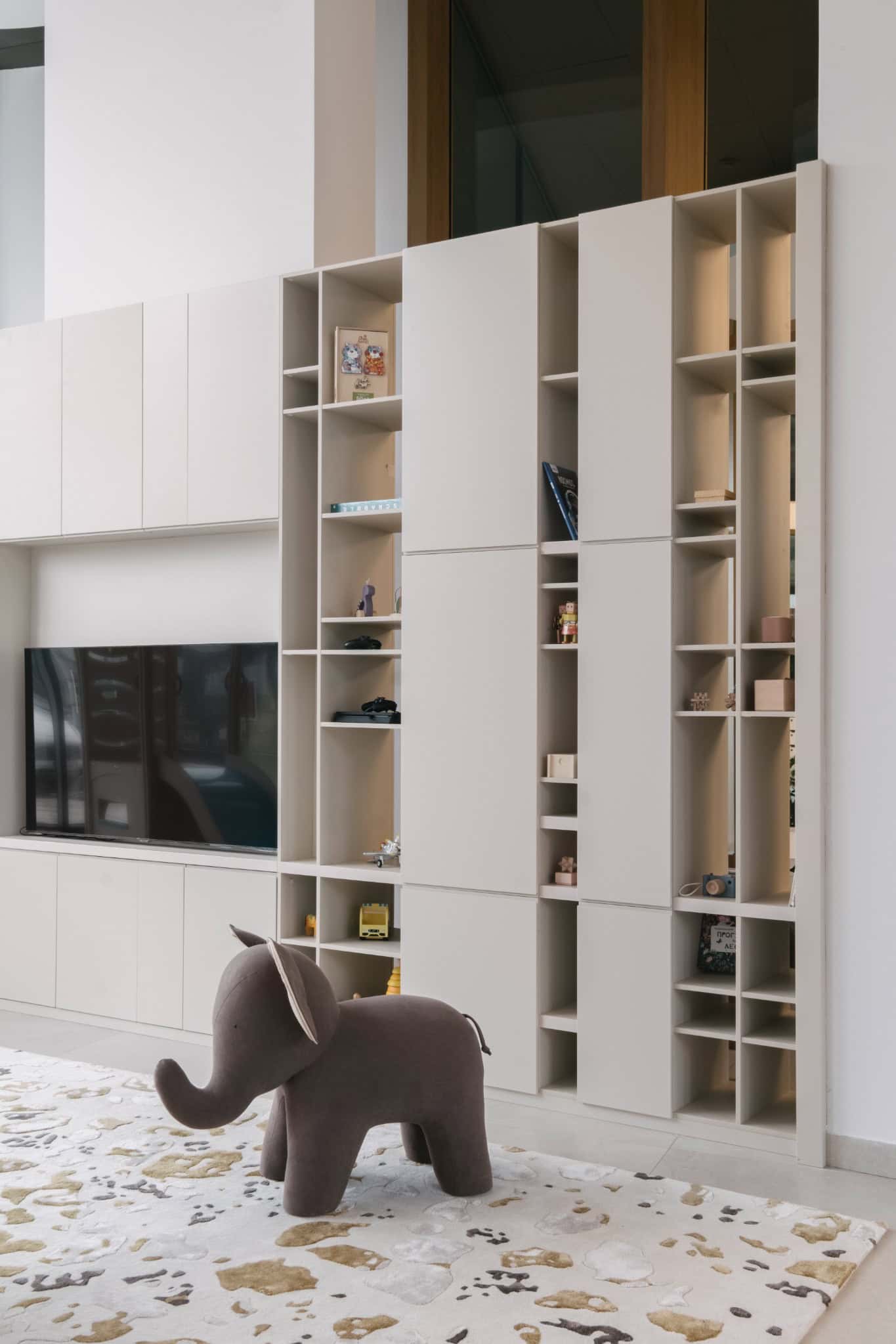 RIVER Kids Playroom Shelving by VSA.studio Scandinavian modern living room with minimalist white built-in shelving and a plush elephant toy, featuring sleek design and functional storage solutions.