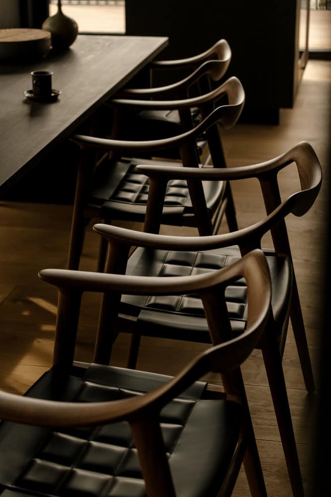 18-07 Holiday Home Chair Lineup Detail by OFFICE INAINN 18-07 Holiday Home by OFFICE INAINN, lineup of sculptural wooden chairs in dining area