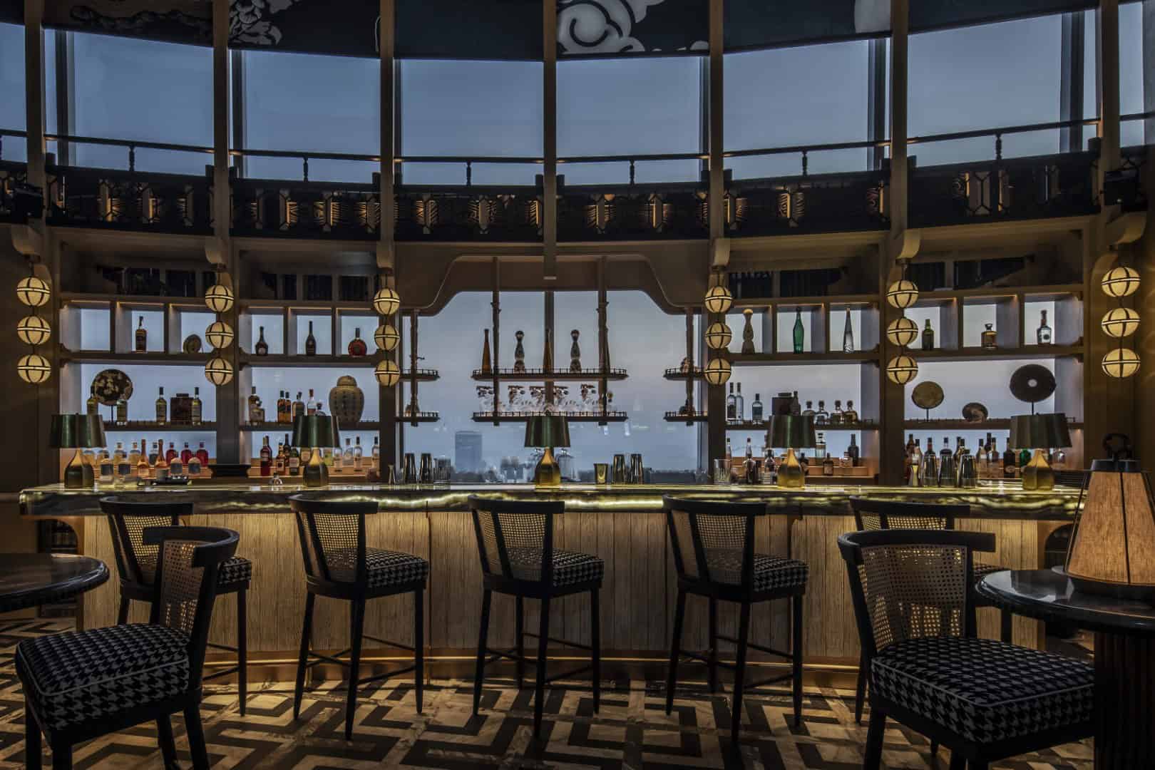 Luxurious modern bar interior with a city view, stylish seating, ambient lighting, and decorative bottles, showcasing contemporary architecture design and upscale hospitality space.