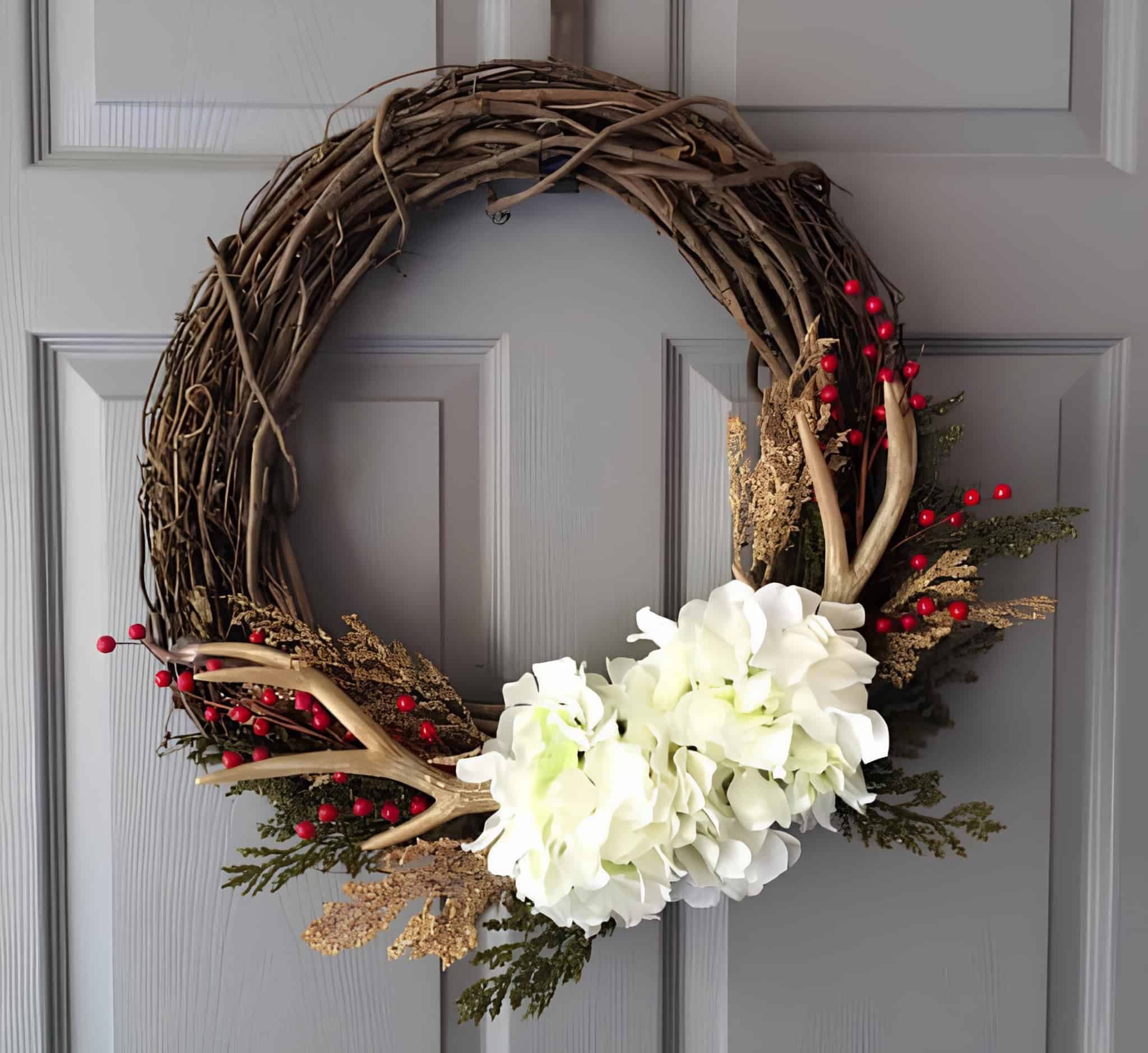 Rustic grapevine wreath with antlers, red berries, greenery and a soft bow around white hydrangeas