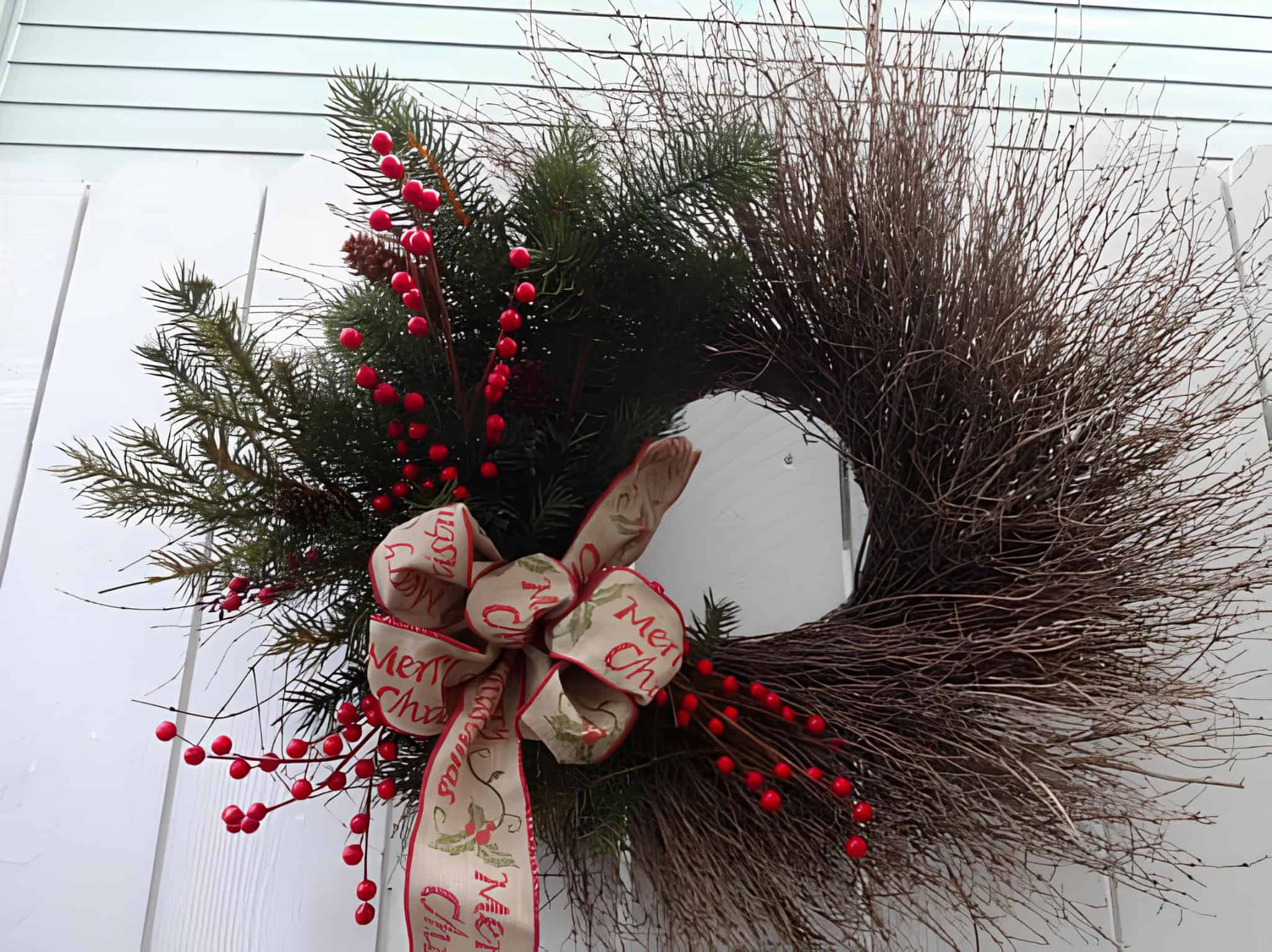 Asymmetrical twig and evergreen Christmas wreath with red berries and Merry Christmas ribbon bow