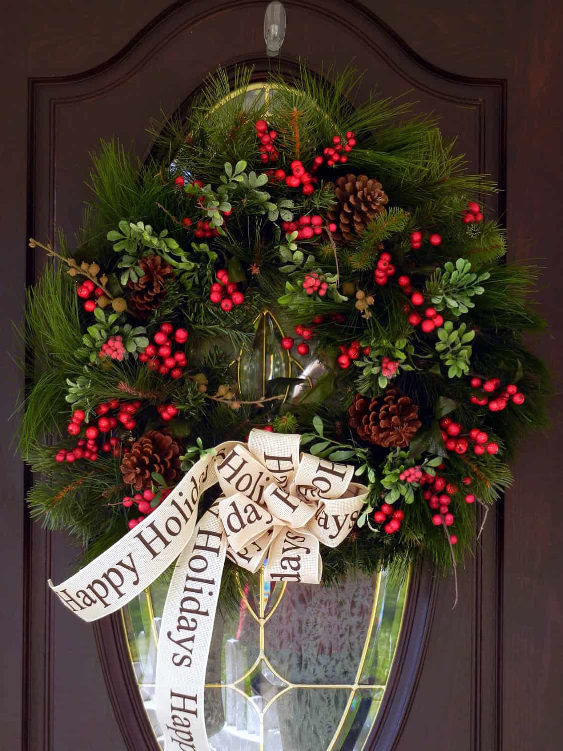 Traditional pine wreath with red berries, pinecones and a Happy Holidays ribbon