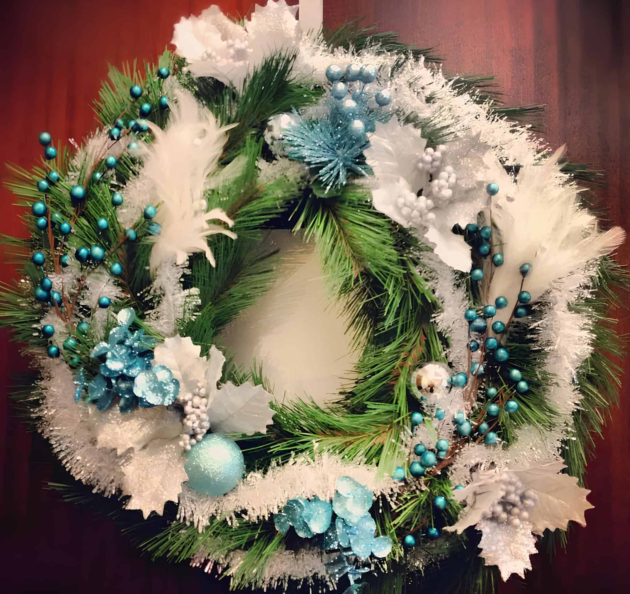 Frosted pine wreath decorated with blue ornaments, white feathers, and icy foliage
