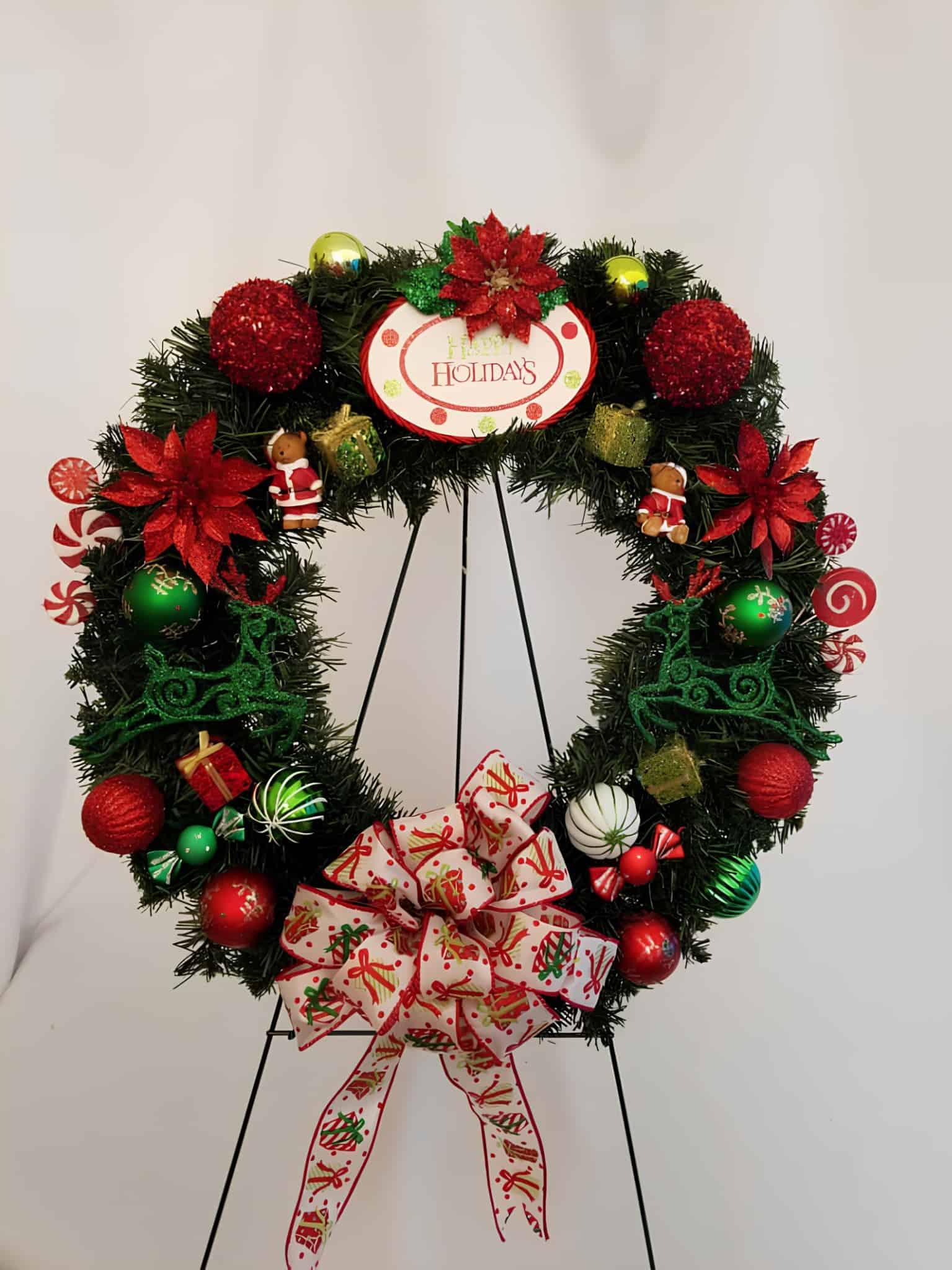 Festive Christmas wreath with red and green ornaments, poinsettias, and a patterned bow