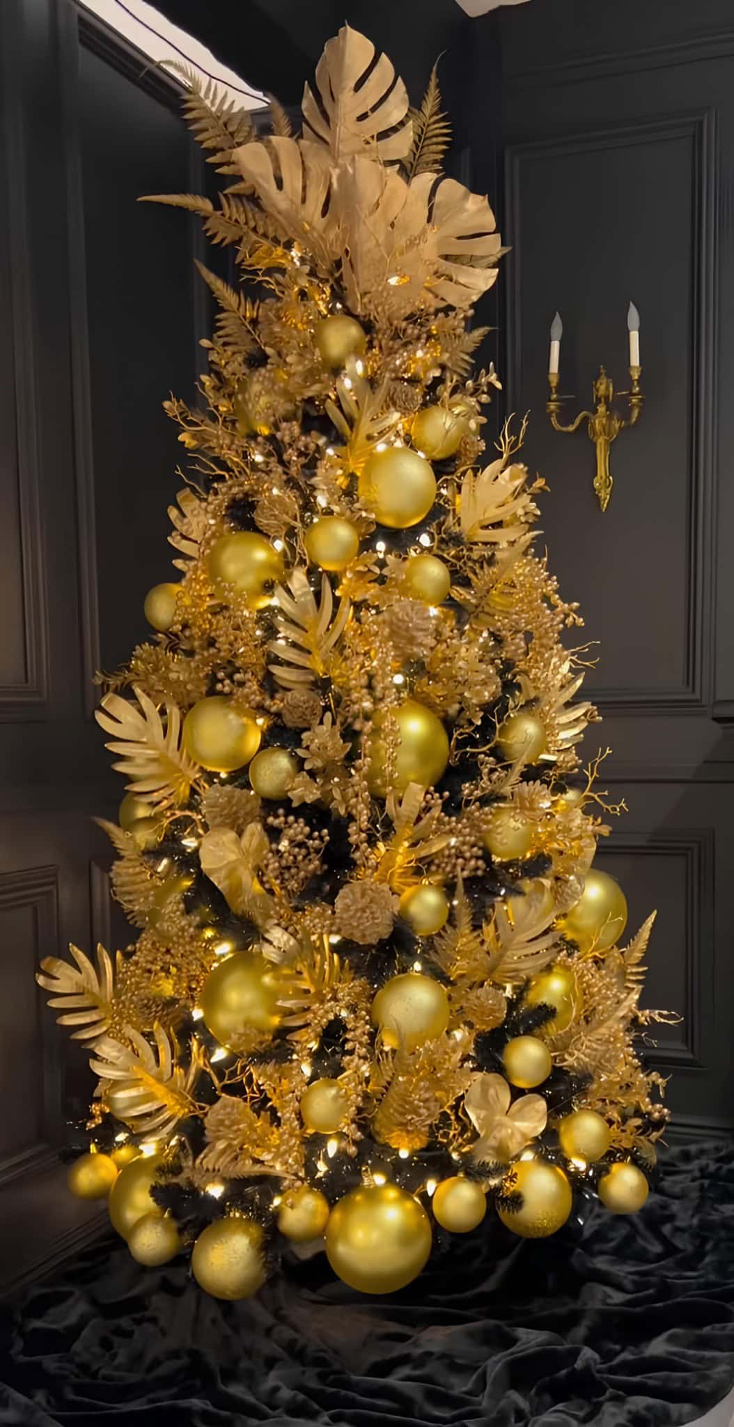 Dramatic black Christmas tree covered in matte and metallic gold ornaments and foliage