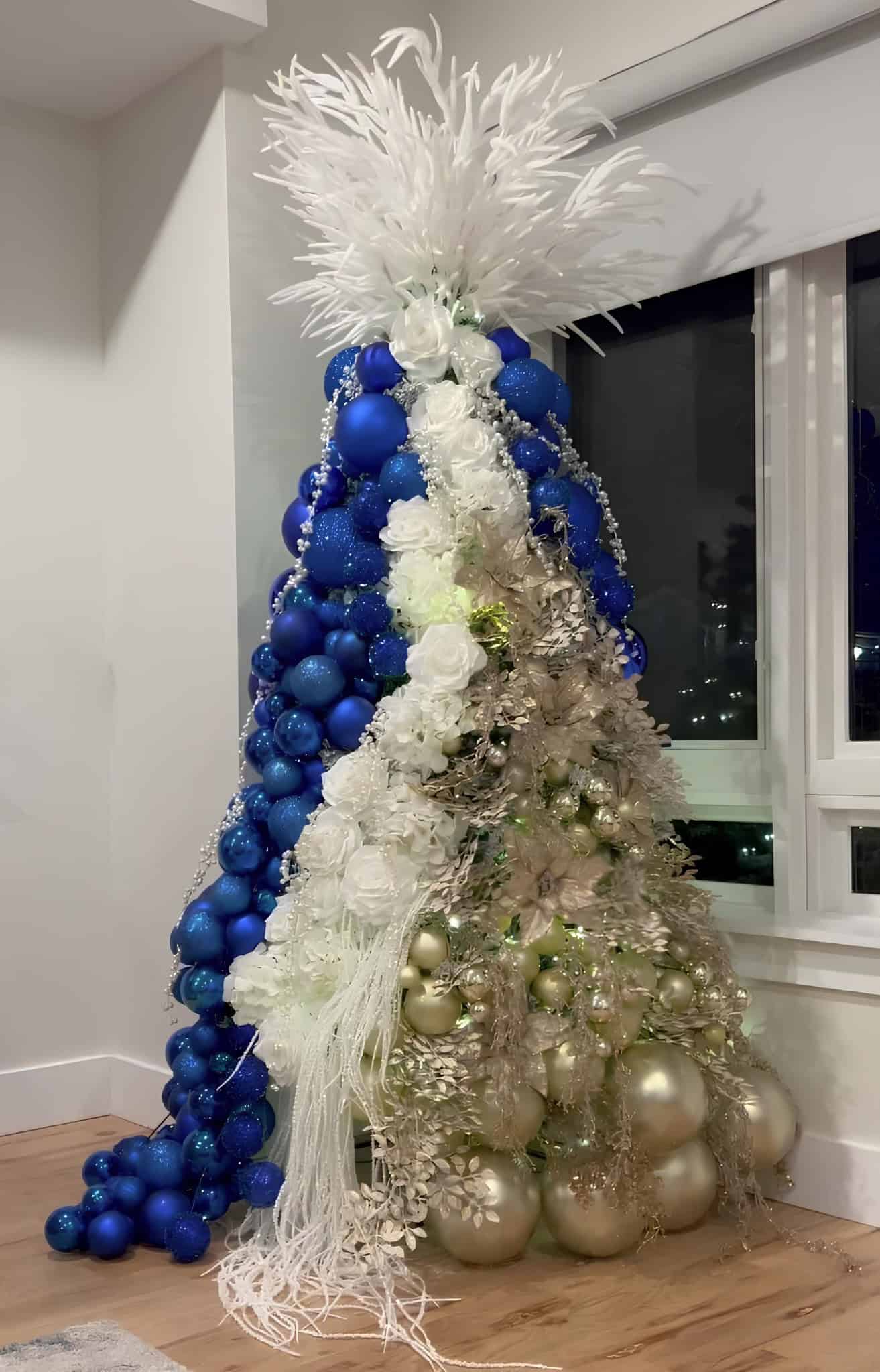 Half blue half white Christmas tree with gold ornaments, florals, and feather topper