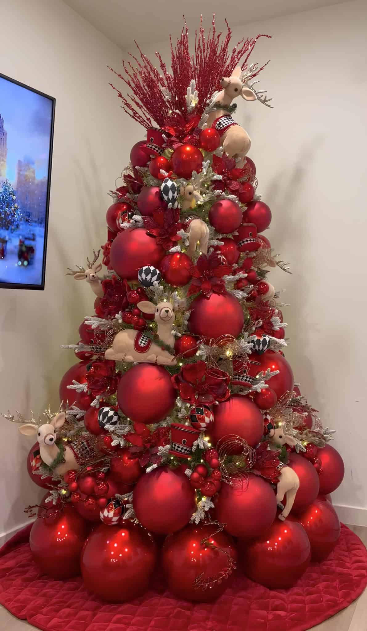 Bold red Christmas tree with oversized ornaments, deer figures, and quilted red tree skirt