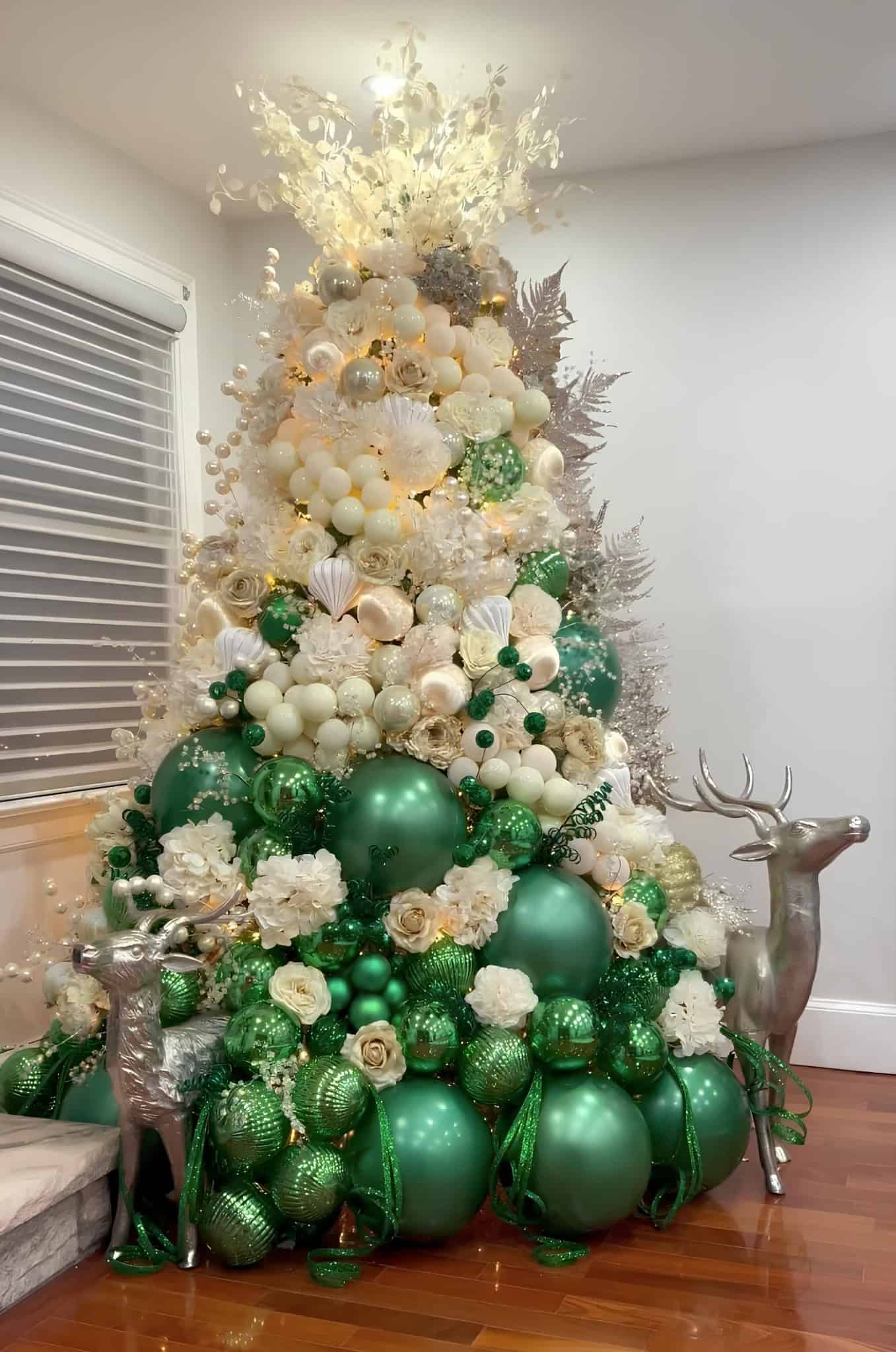 Emerald green and ivory Christmas tree with oversized ornaments, white florals, and silver deer accents