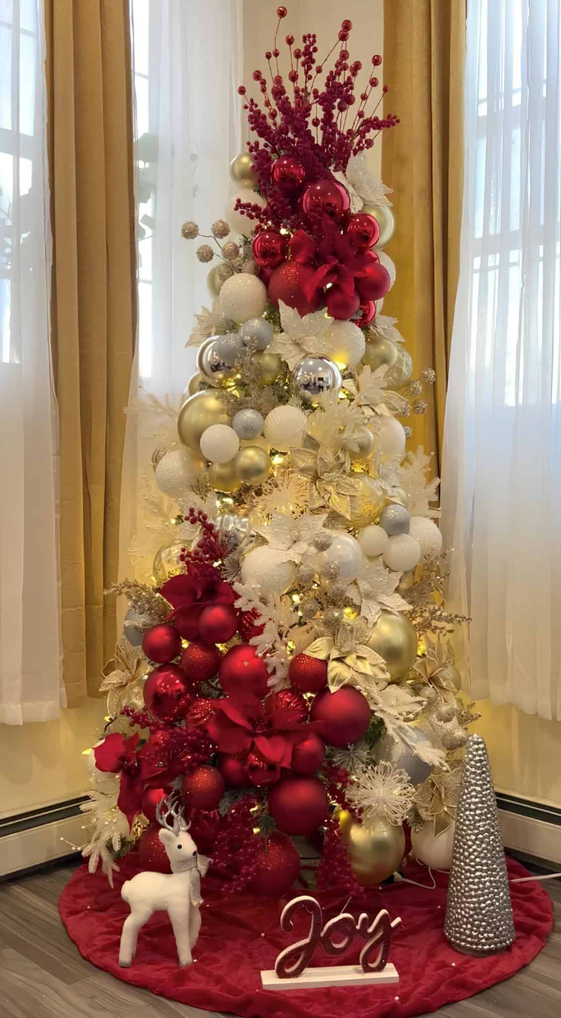 Red and gold Christmas tree with poinsettias, berries, and metallic ornaments on a white-gold base