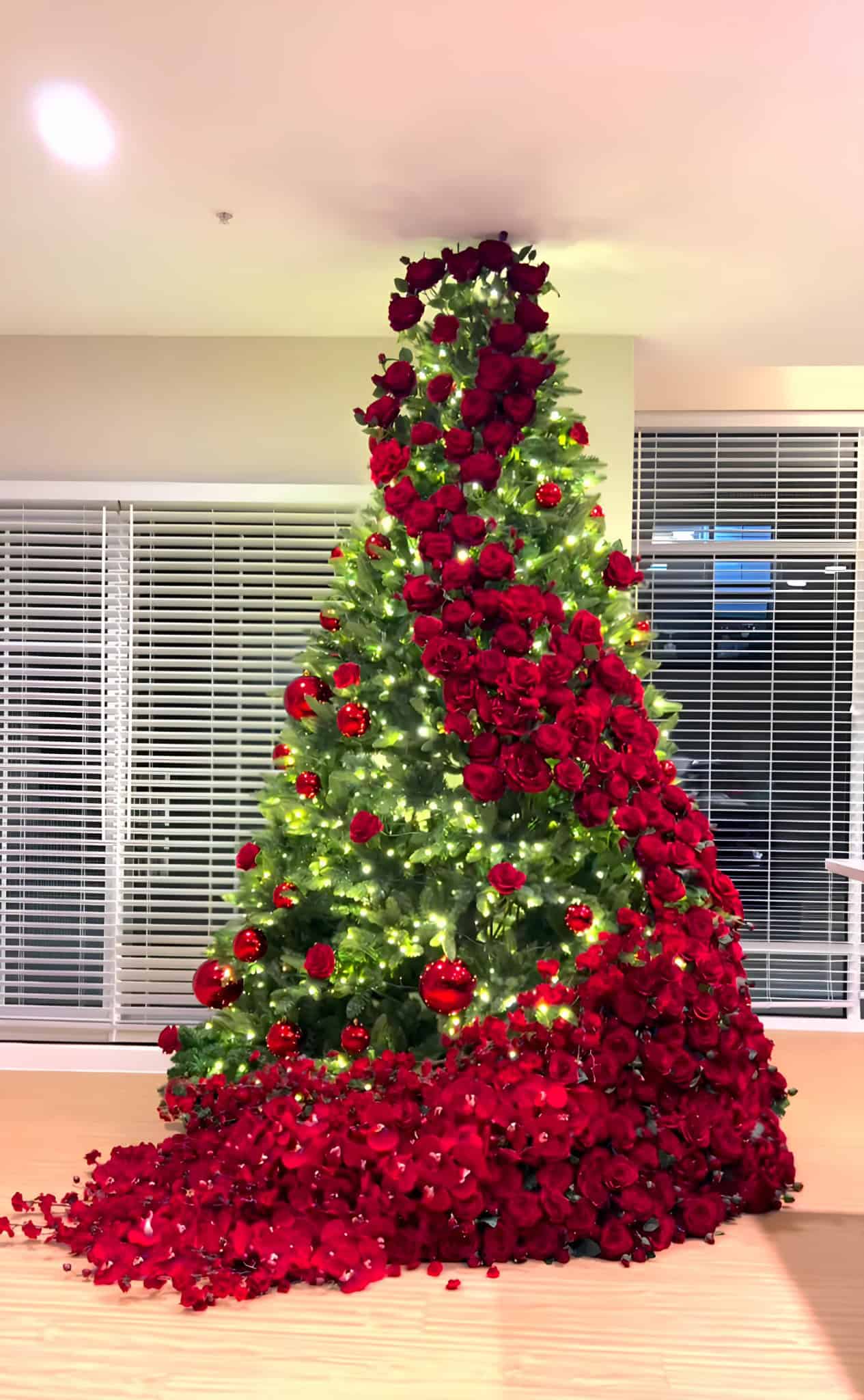 Luxurious Christmas tree draped in cascading red roses with warm lights and a petal skirt