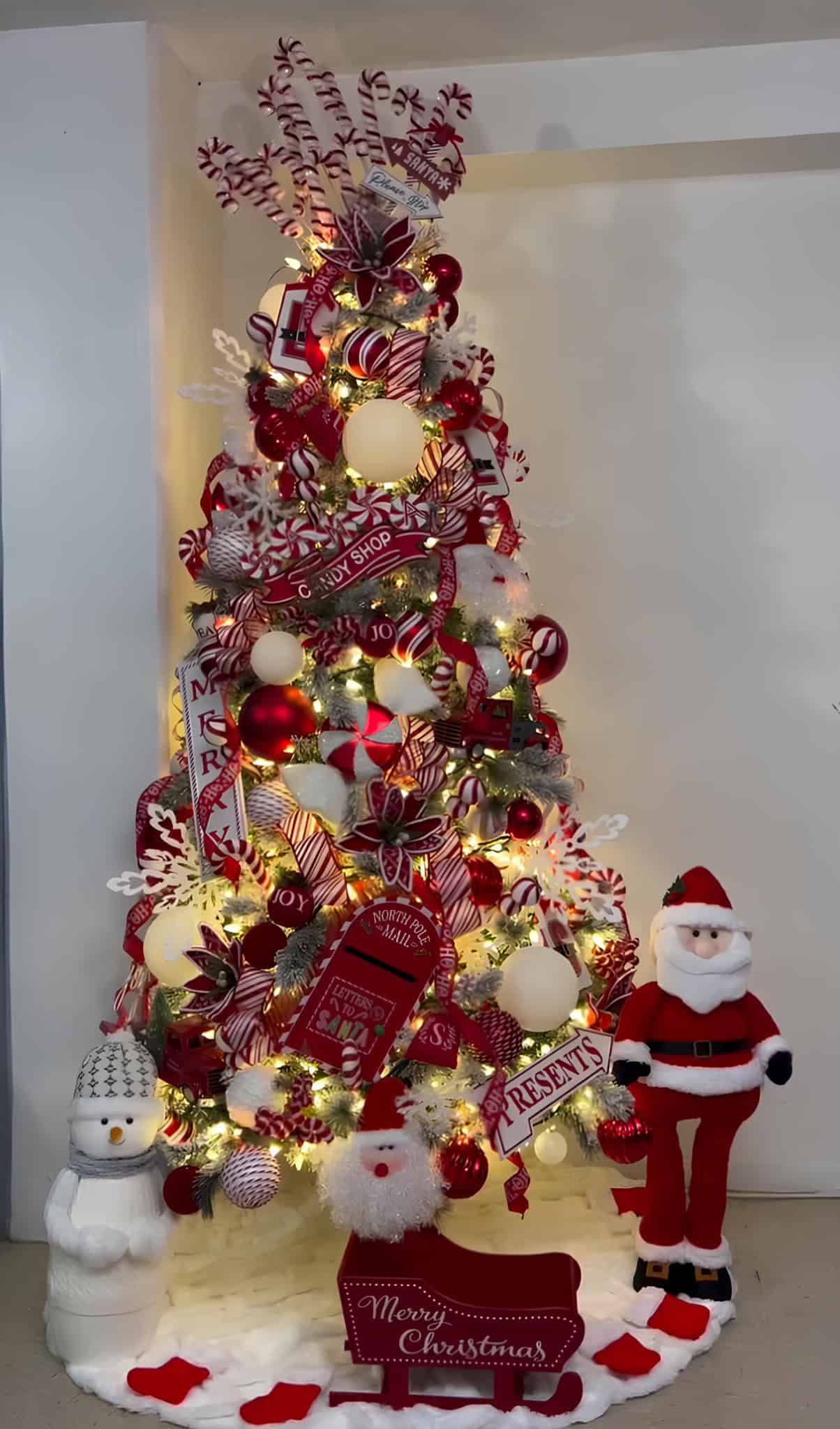 Red and white peppermint candy Christmas tree with ribbons, signs, and lollipop ornaments