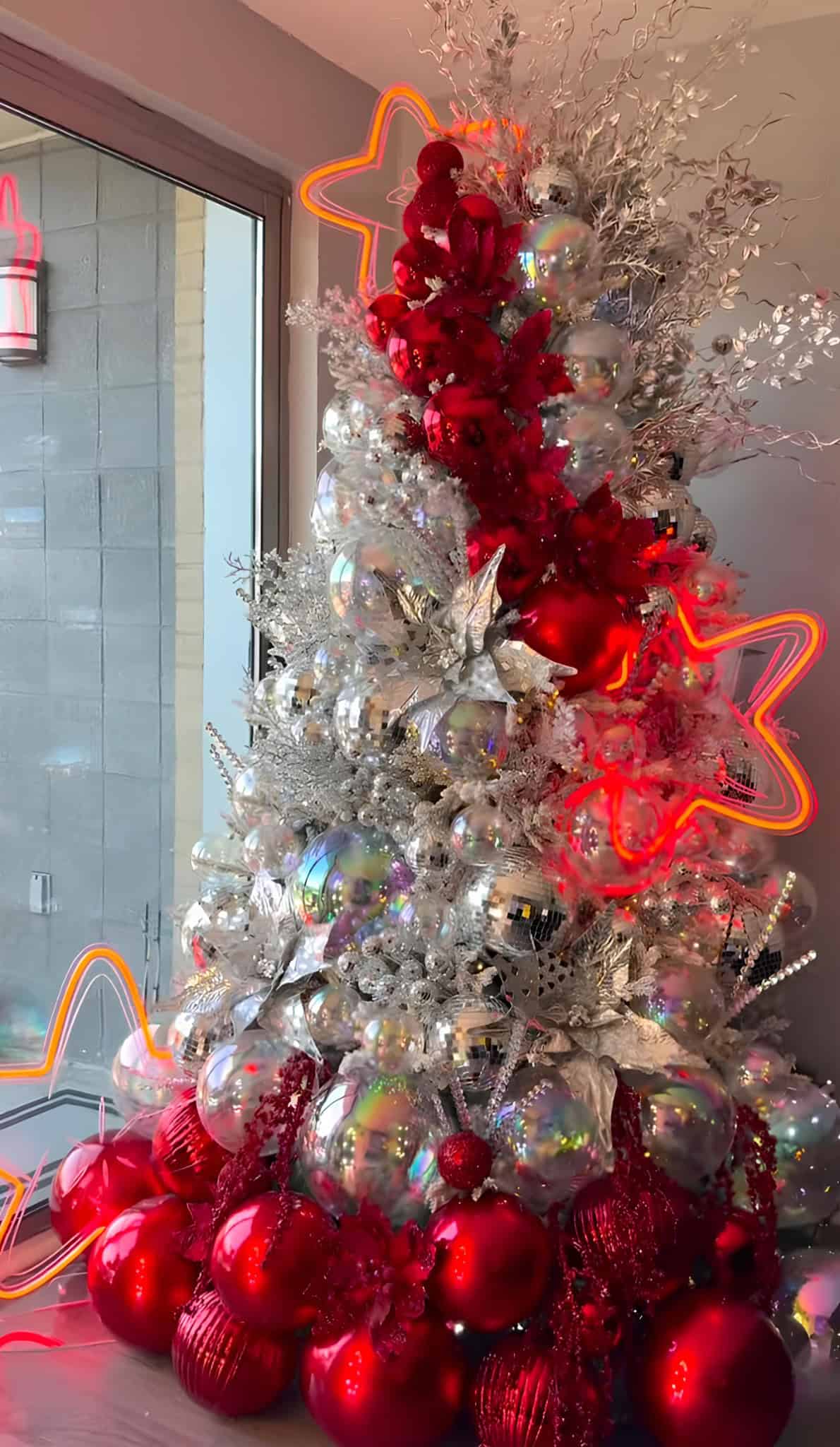 Silver Christmas tree with red ornaments, neon star lights, and disco-ball shine
