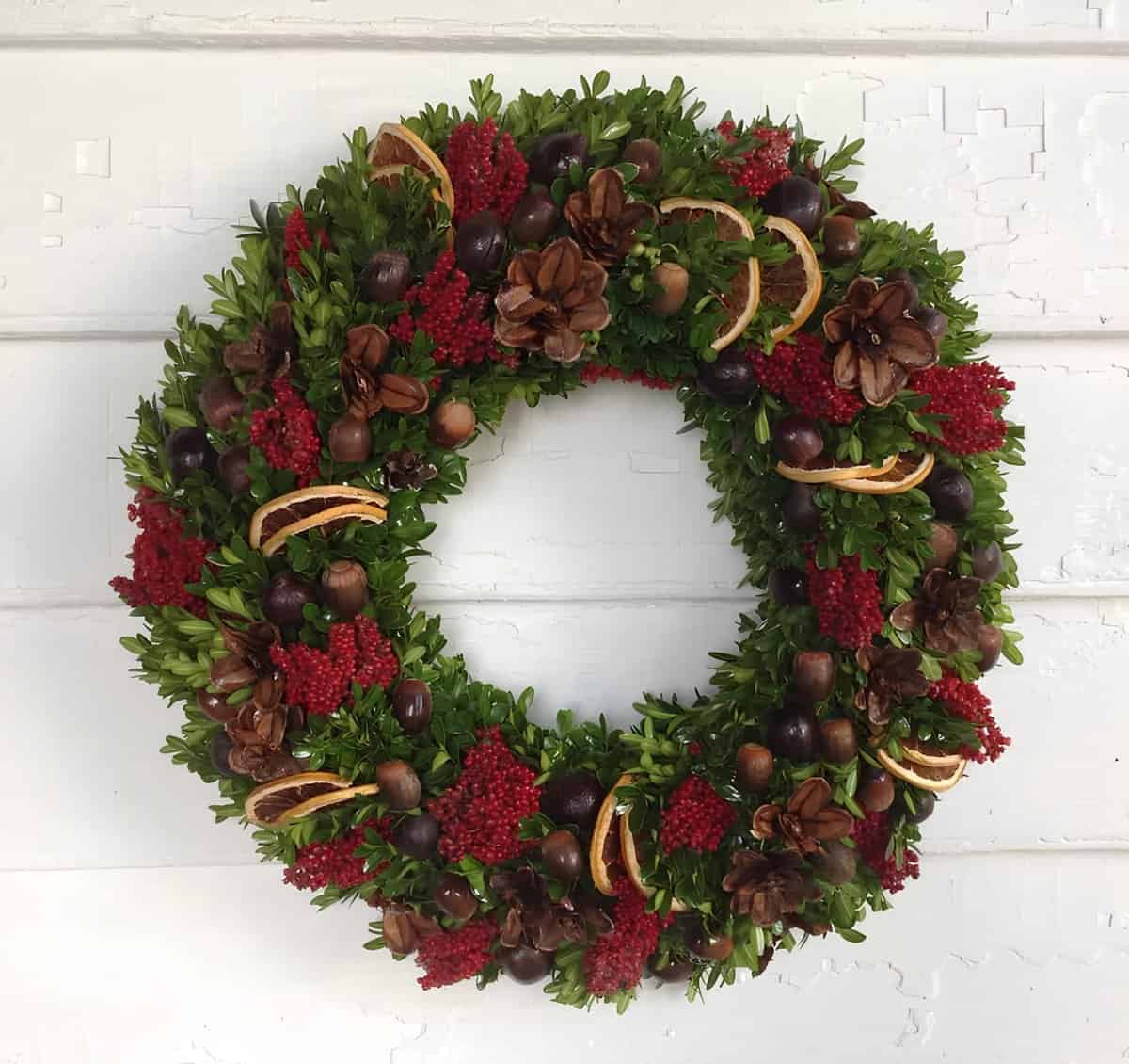 Boxwood Christmas wreath with red berries, pinecones, acorns, and dried orange slices
