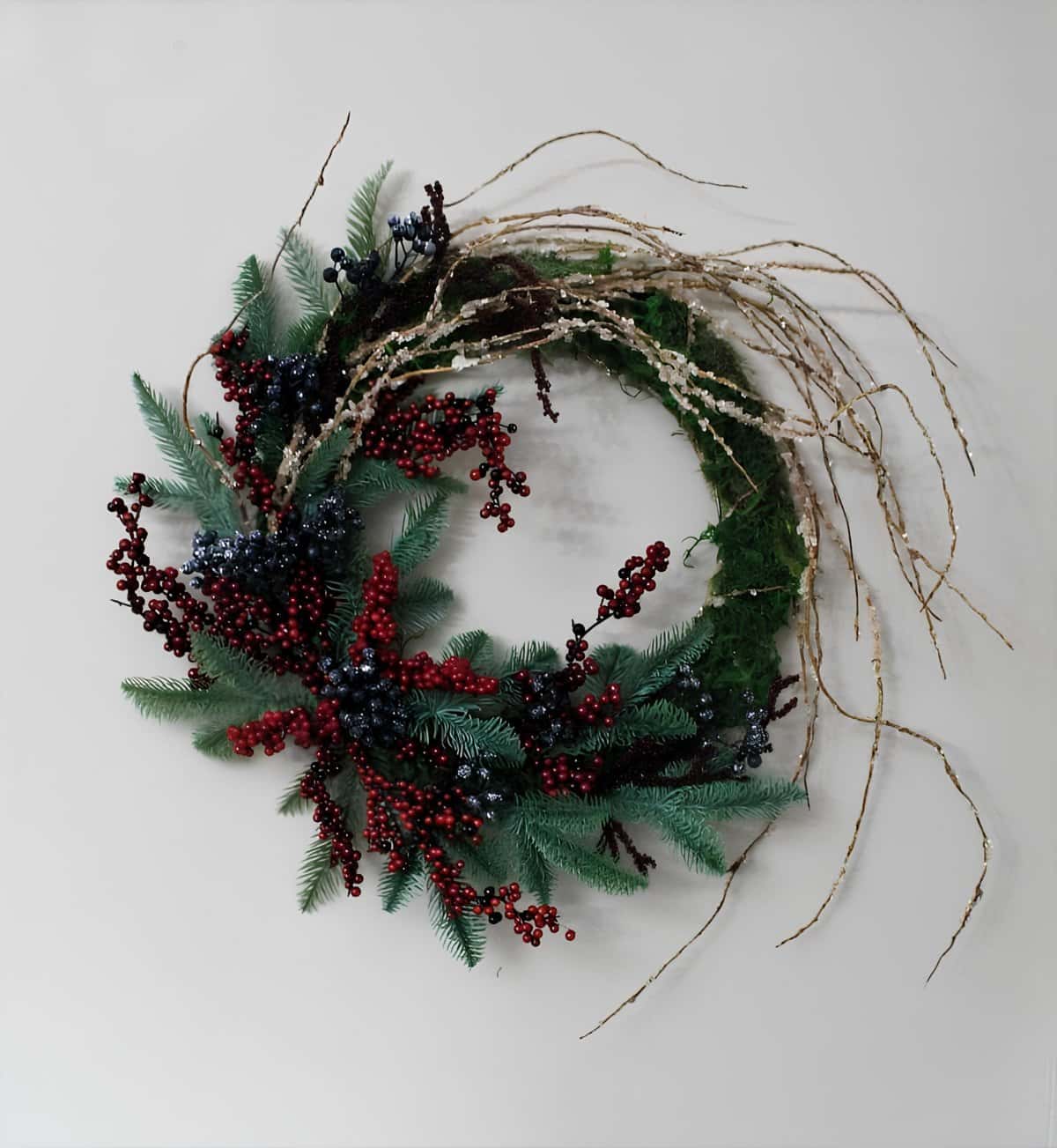 Asymmetrical twig wreath with evergreens and clusters of red and blue berries