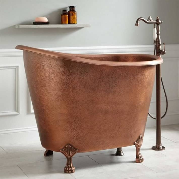 Vintage hammered copper clawfoot soaking tub in a classic bathroom with freestanding faucet